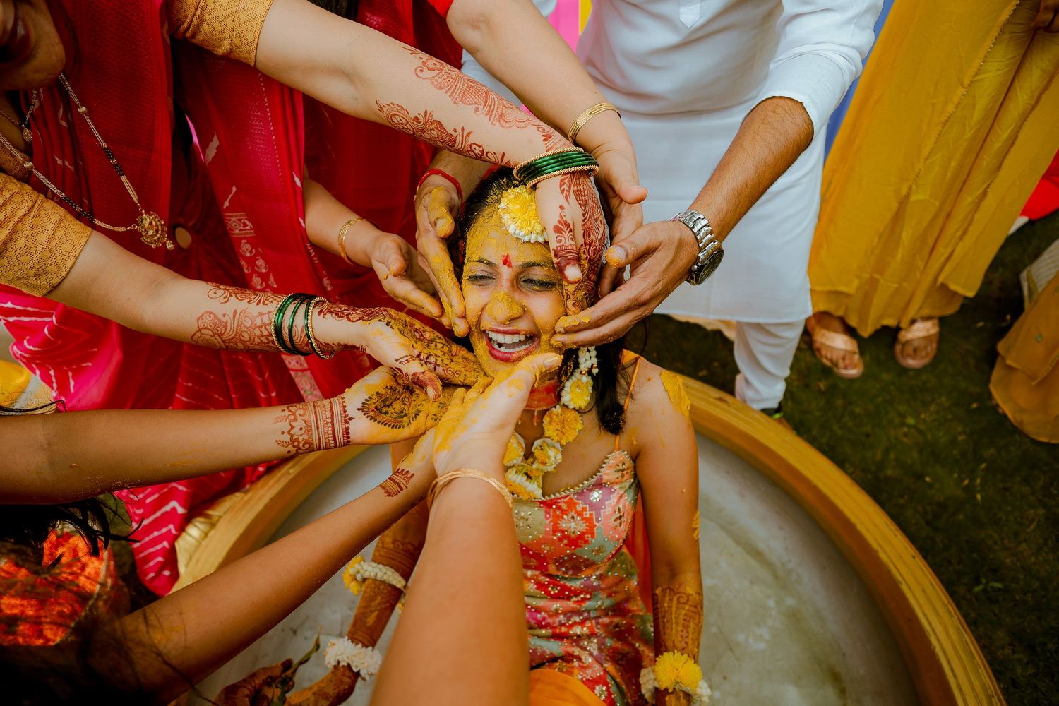 Traditional Indian wedding ceremony shows hands applying turmeric paste during Haldi ritual celebration.