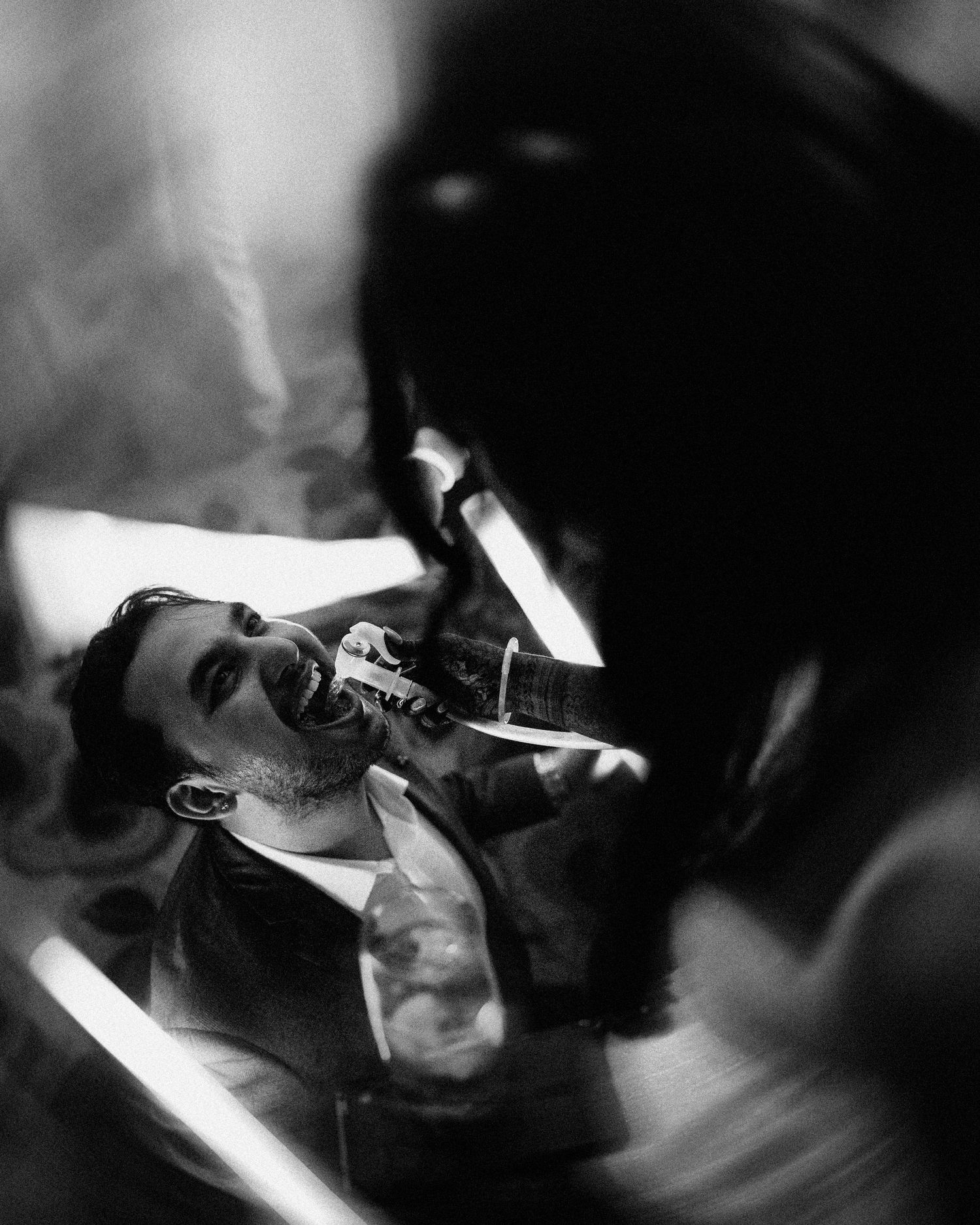 Black and white photo of a man lying back while another person holds a microphone to his mouth.