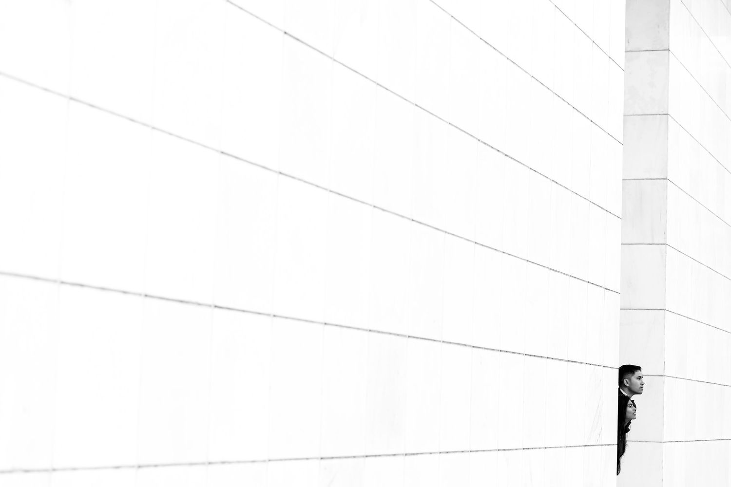A person peeks around a white minimalist wall corner in a striking black and white architectural photograph.