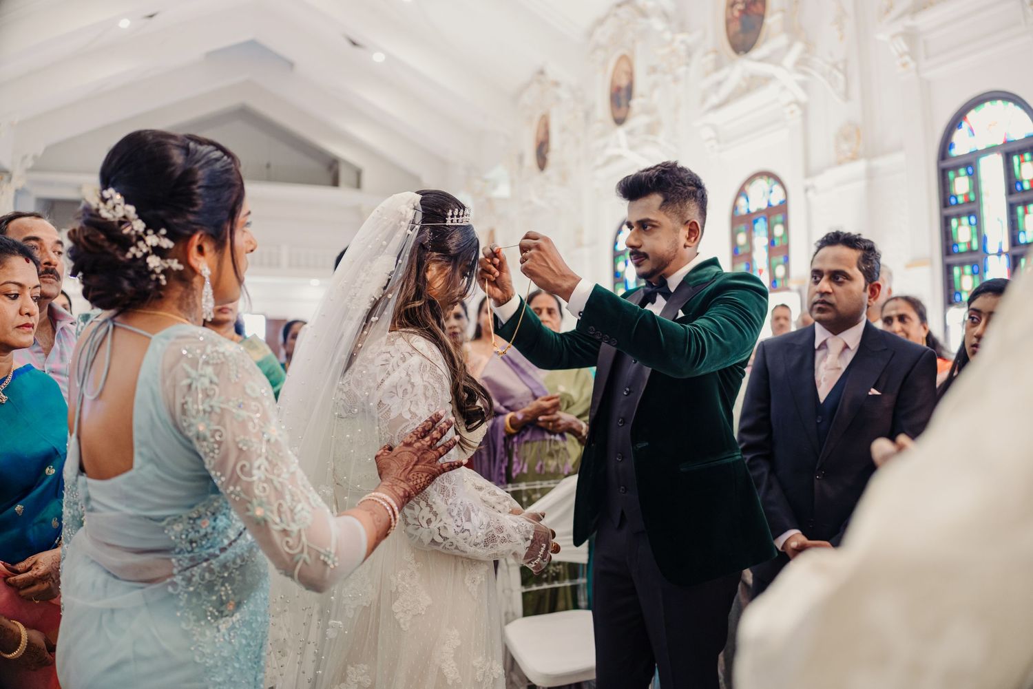 Wedding guests celebrate during a joyful reception in an elegant white-walled venue with ornate decorations.