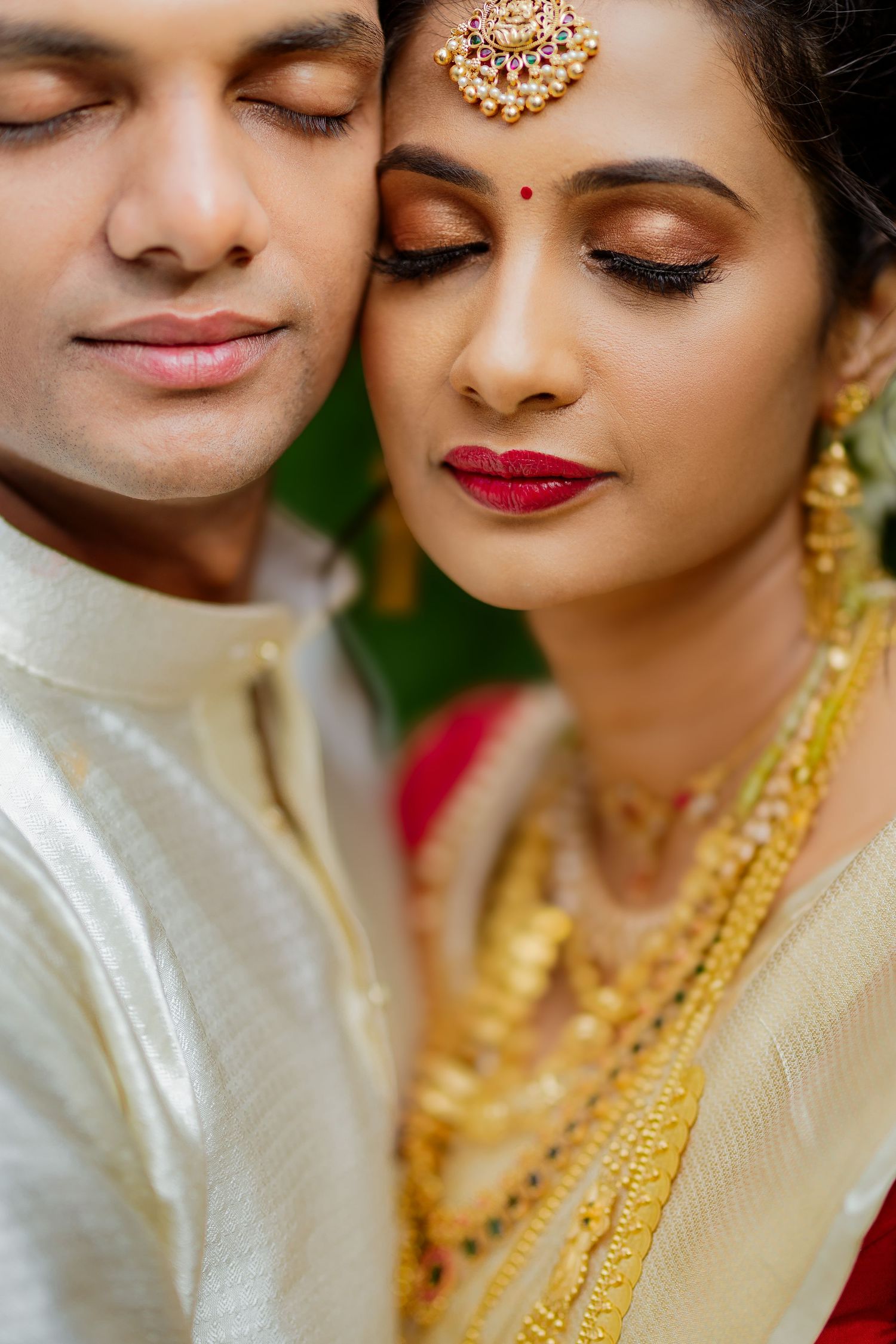 Close-up portrait of an Indian couple in traditional wedding attire with gold jewelry and bridal makeup.