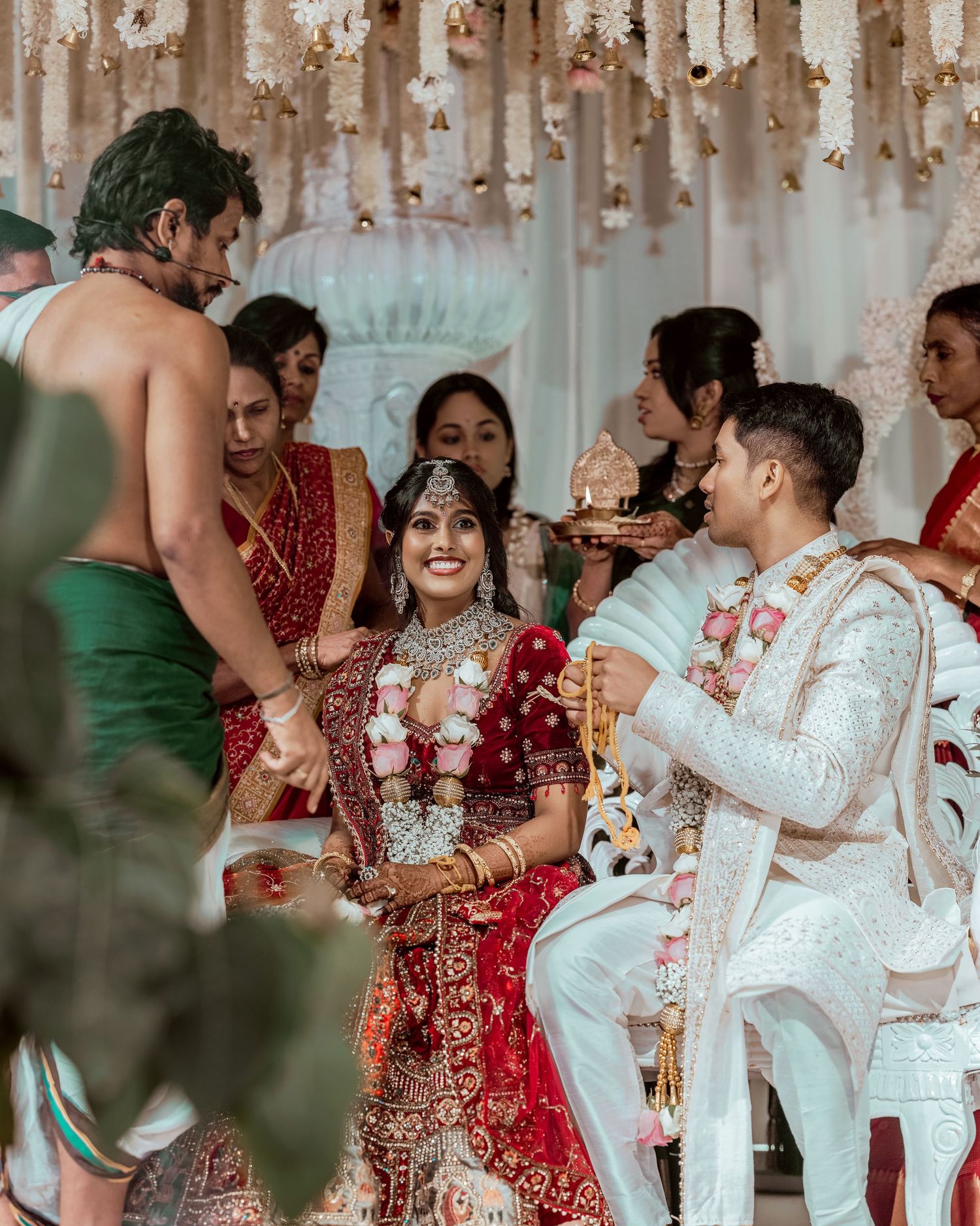 A bride in red lehenga and groom in white sherwani during a traditional Indian Hindu wedding ceremony with floral decorations.