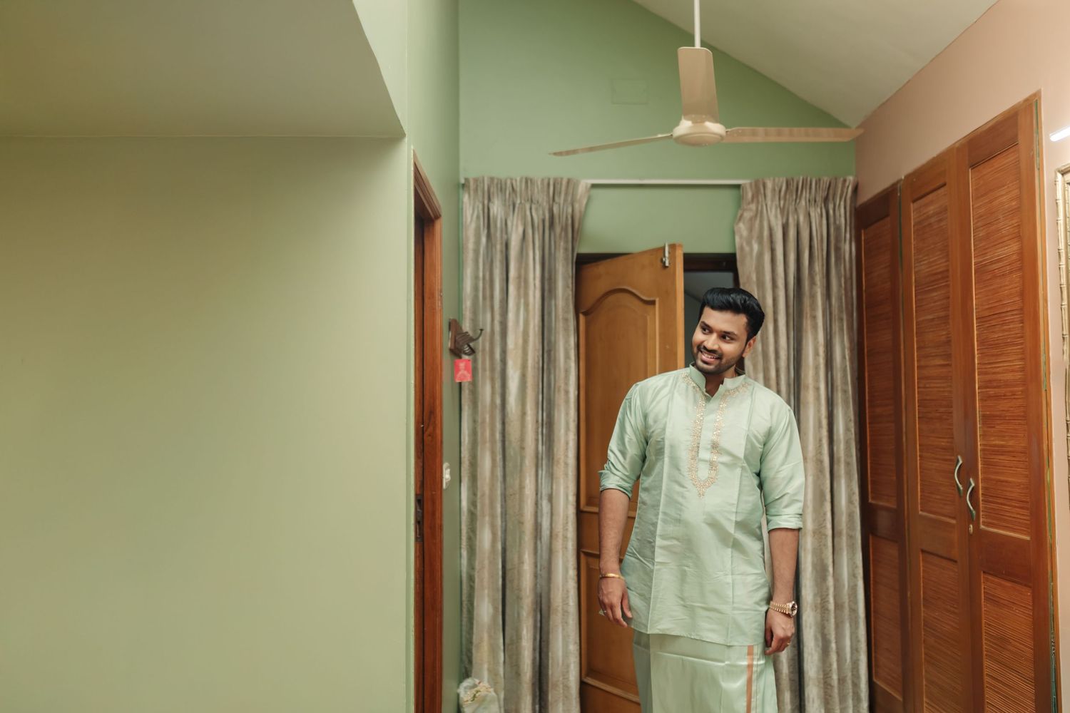 Person wearing a light mint green traditional Indian outfit stands in a doorway.
