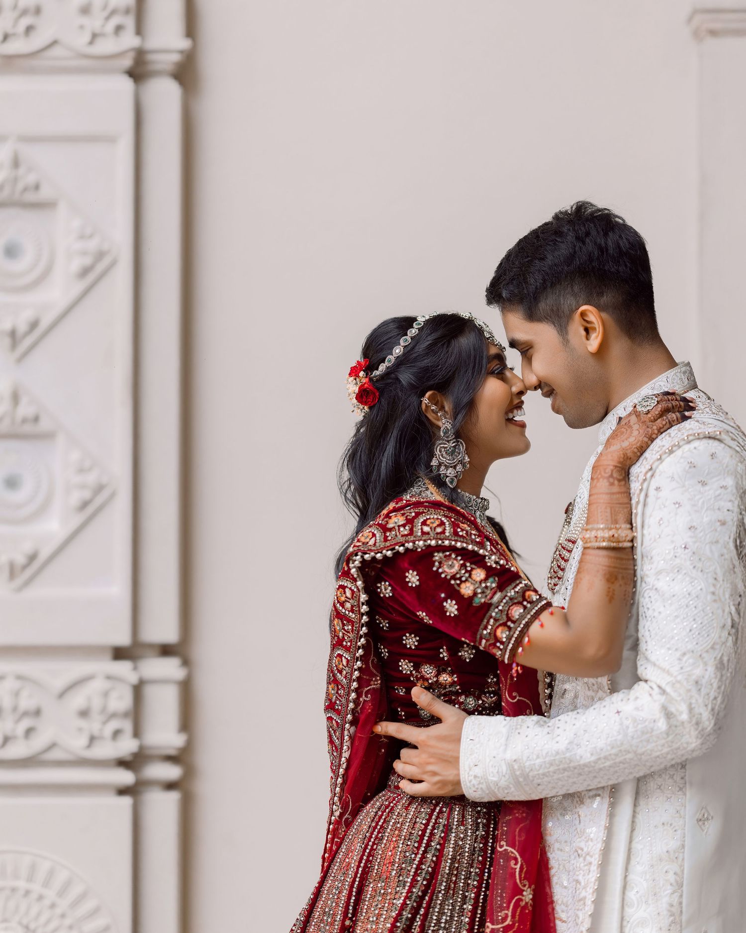 Indian couple in traditional wedding attire, bride in red lehenga and groom in white sherwani, sharing an intimate moment.