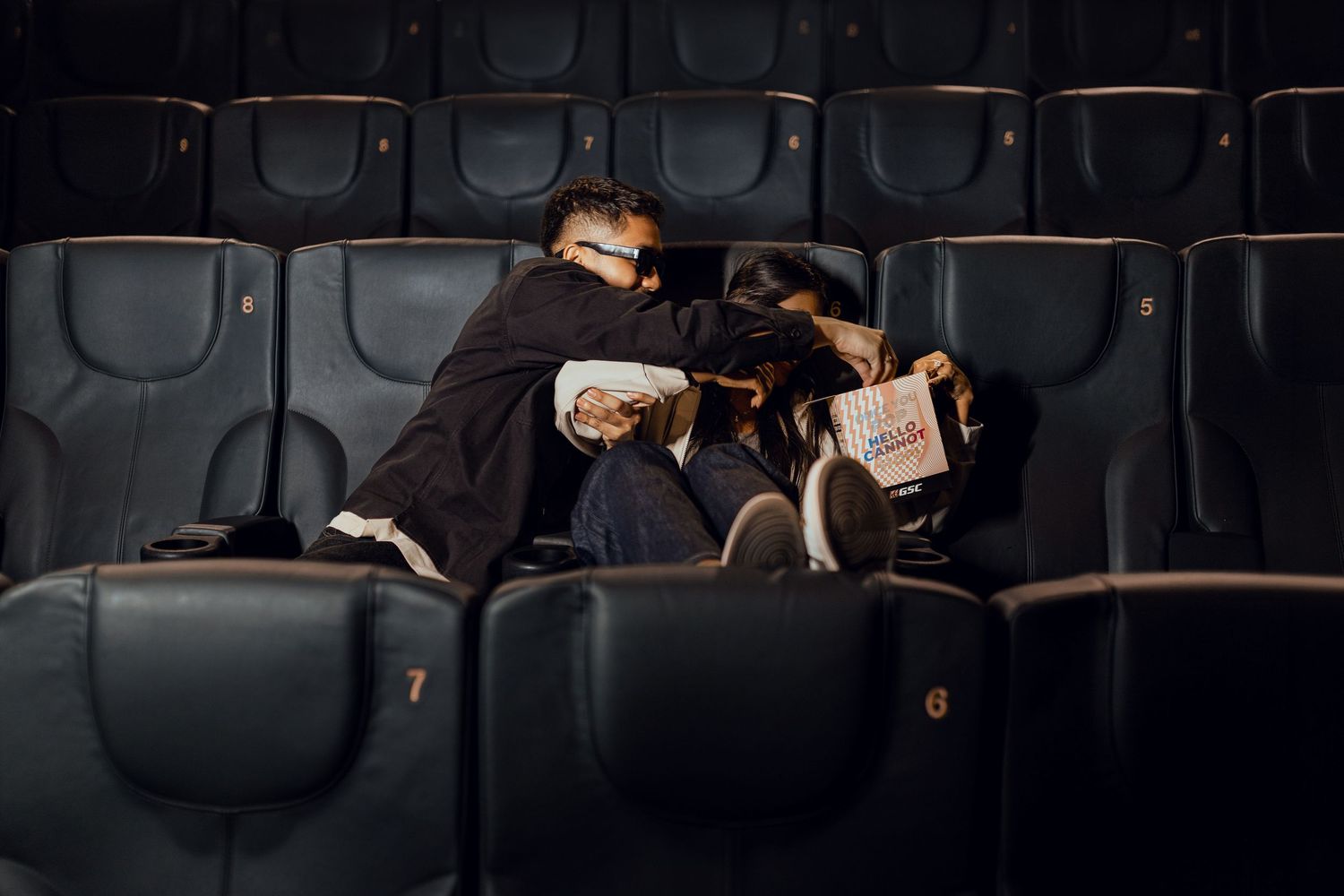 Couple cuddling in empty movie theater seats, sharing popcorn during a romantic cinema date night.