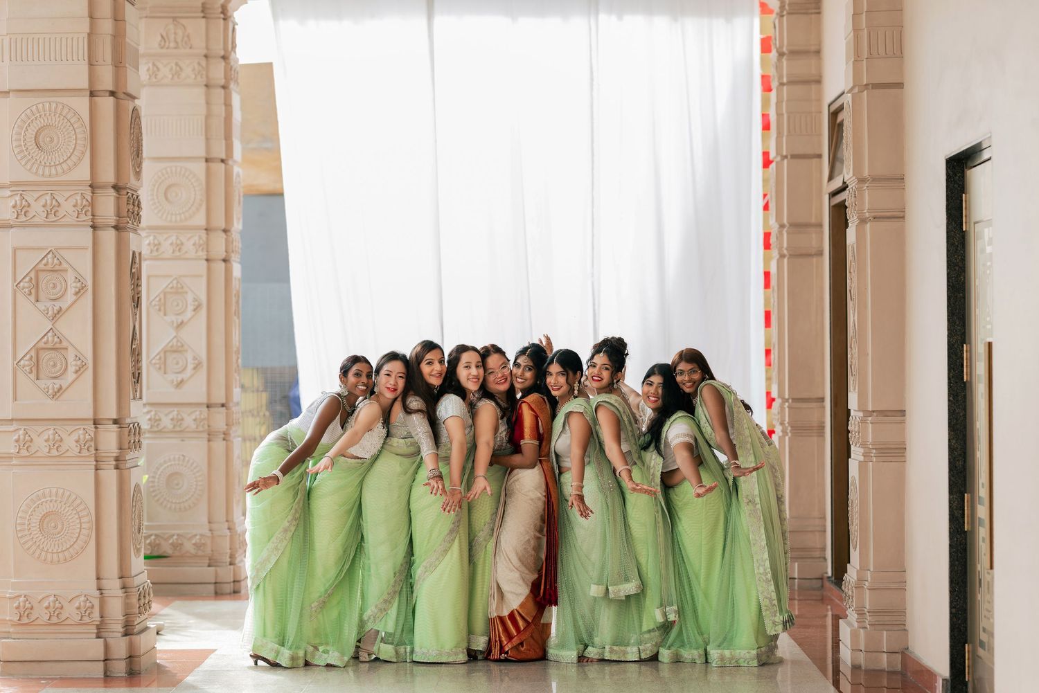 Bridesmaids in mint green sarees posing together at an Indian wedding venue with ornate architecture.