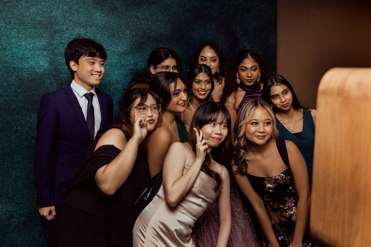 Group of young adults posing together in formal attire at an elegant event, smiling and making fun poses.
