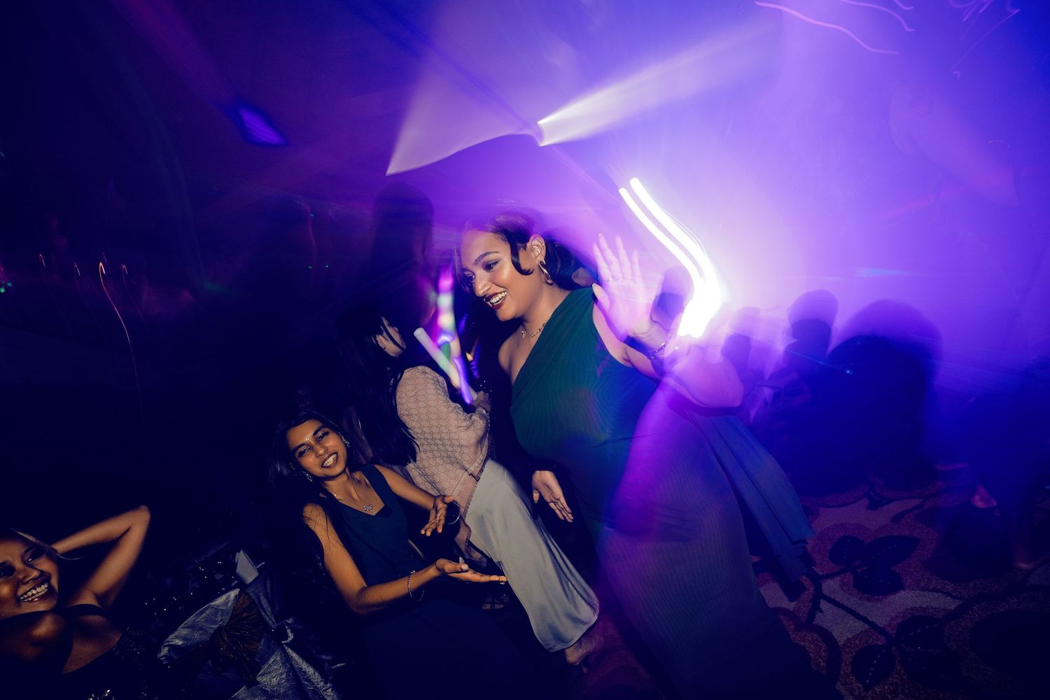 Women dancing and socializing at a vibrant nightclub with purple and neon lights.
