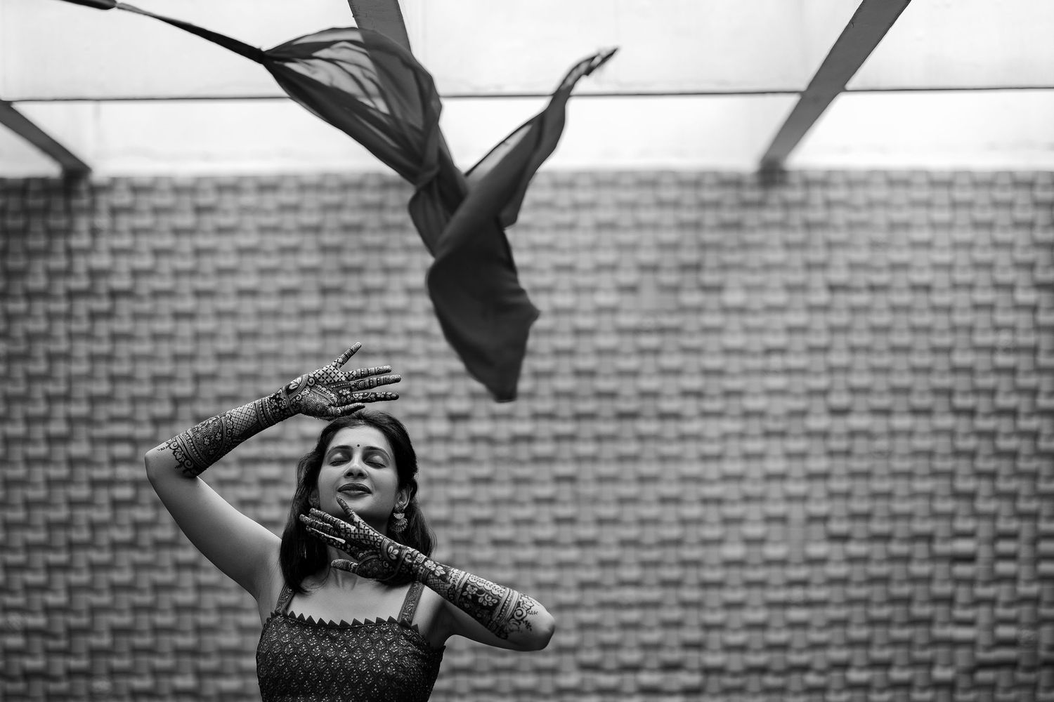 A dancer performs an expressive pose in front of a brick wall while a fabric flows dramatically above in black and white.
