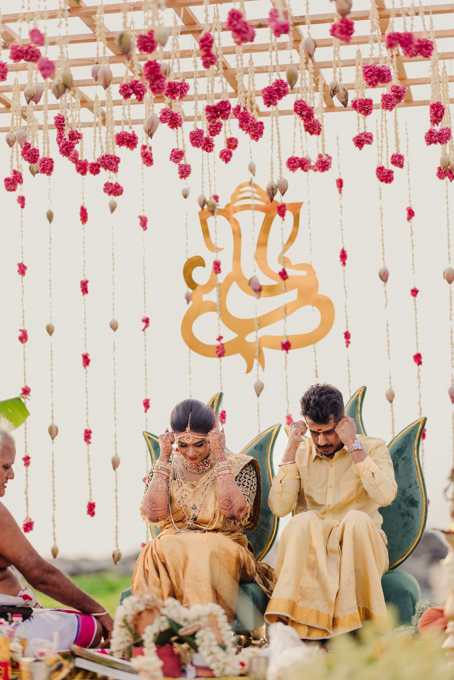 Traditional Indian wedding ceremony under pink floral decor and golden calligraphy decorations.