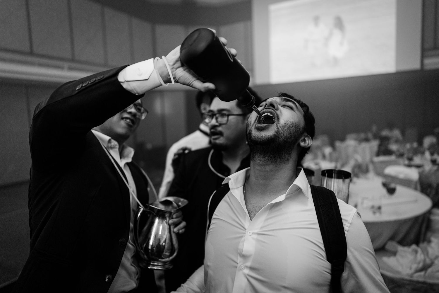 Black and white photo of men laughing and pouring drinks at a festive indoor celebration event.