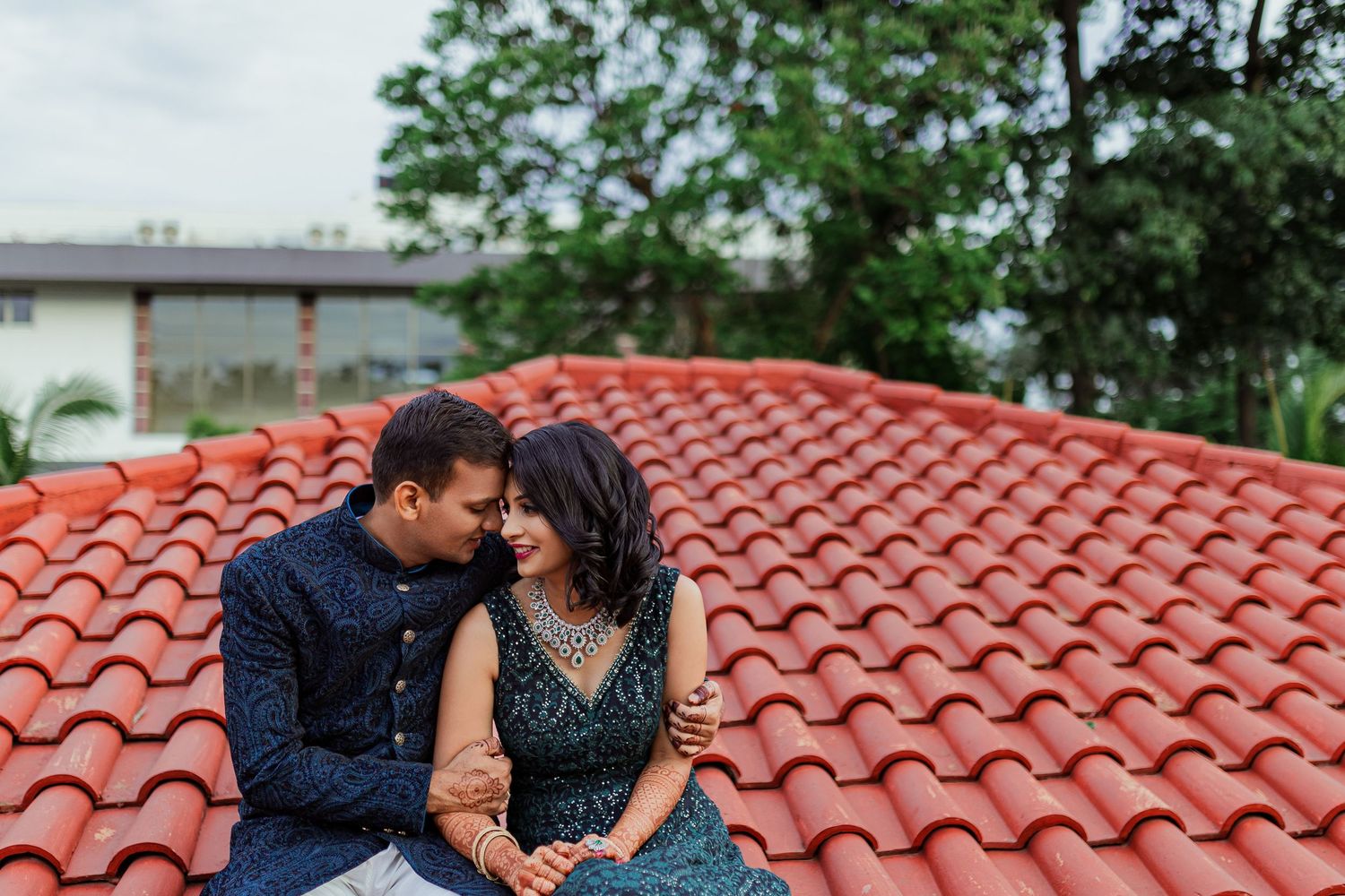 A couple shares a romantic moment together on a Spanish tile roof with trees in the background.