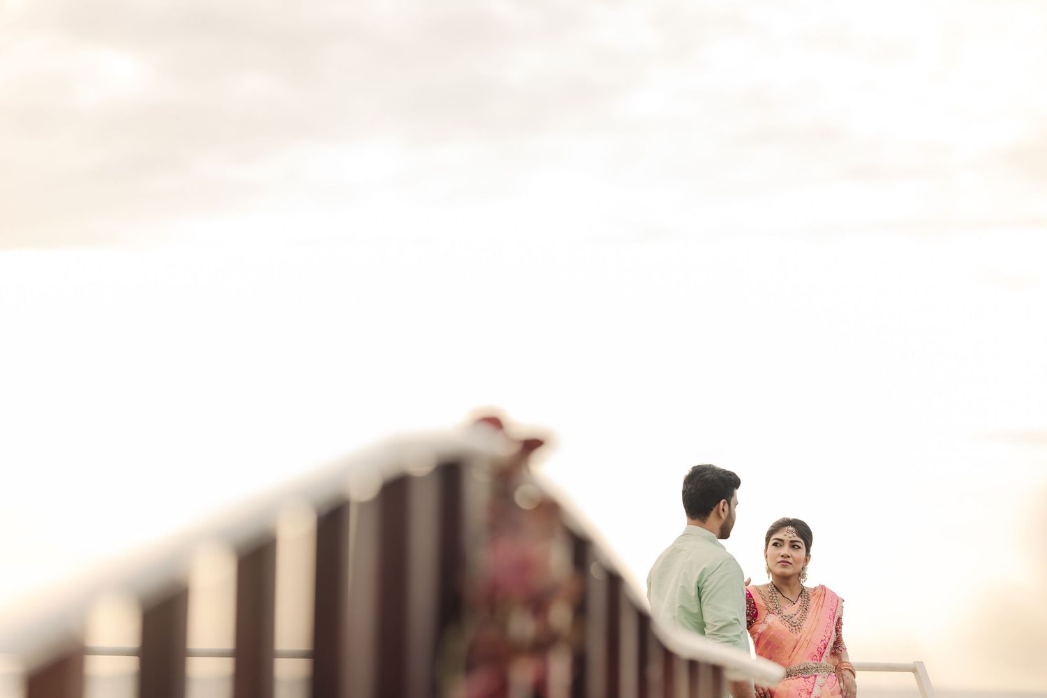 Romantic beach photoshoot at sunset with couple in pink and mint green traditional Indian outfits.