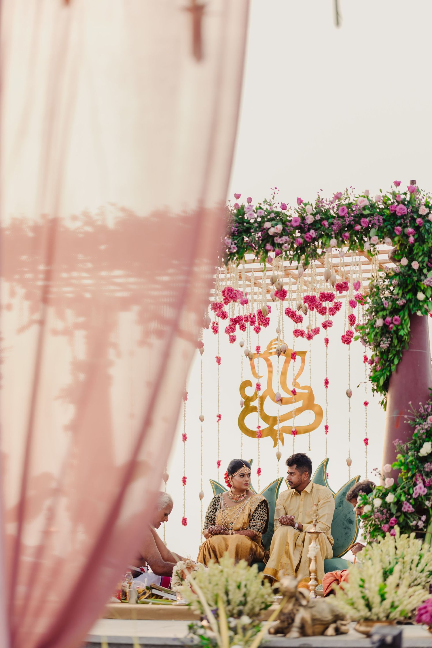 Wedding ceremony setup with pink flowers and golden decorations against a white backdrop.