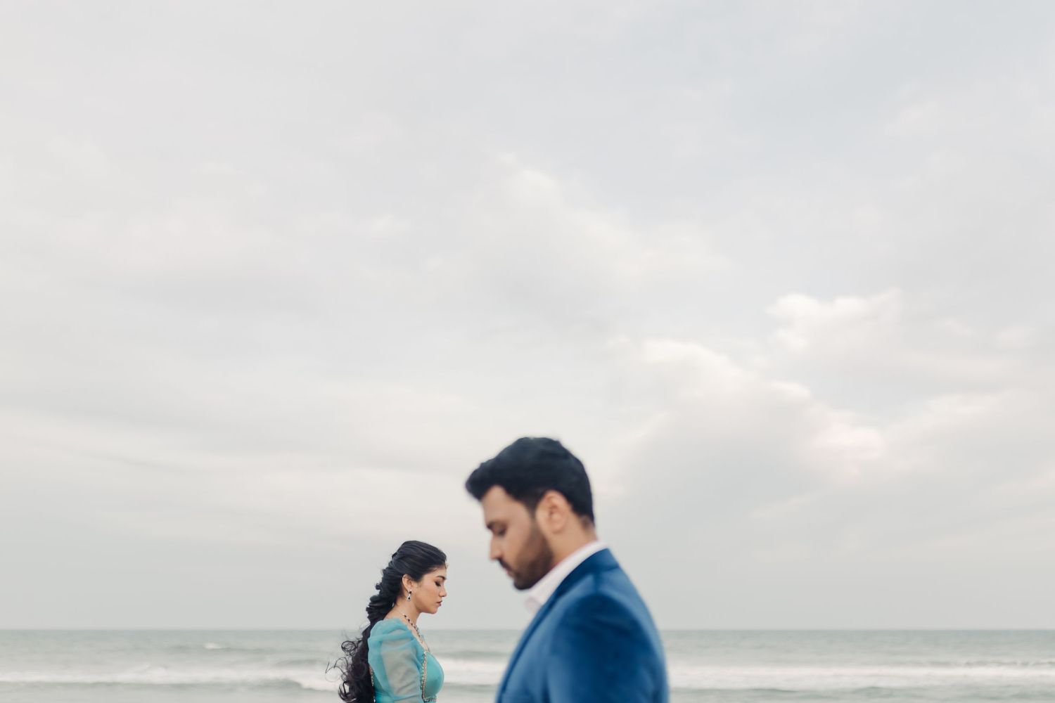 A couple walks along a misty beach shore during an overcast day with waves rolling in from the ocean.
