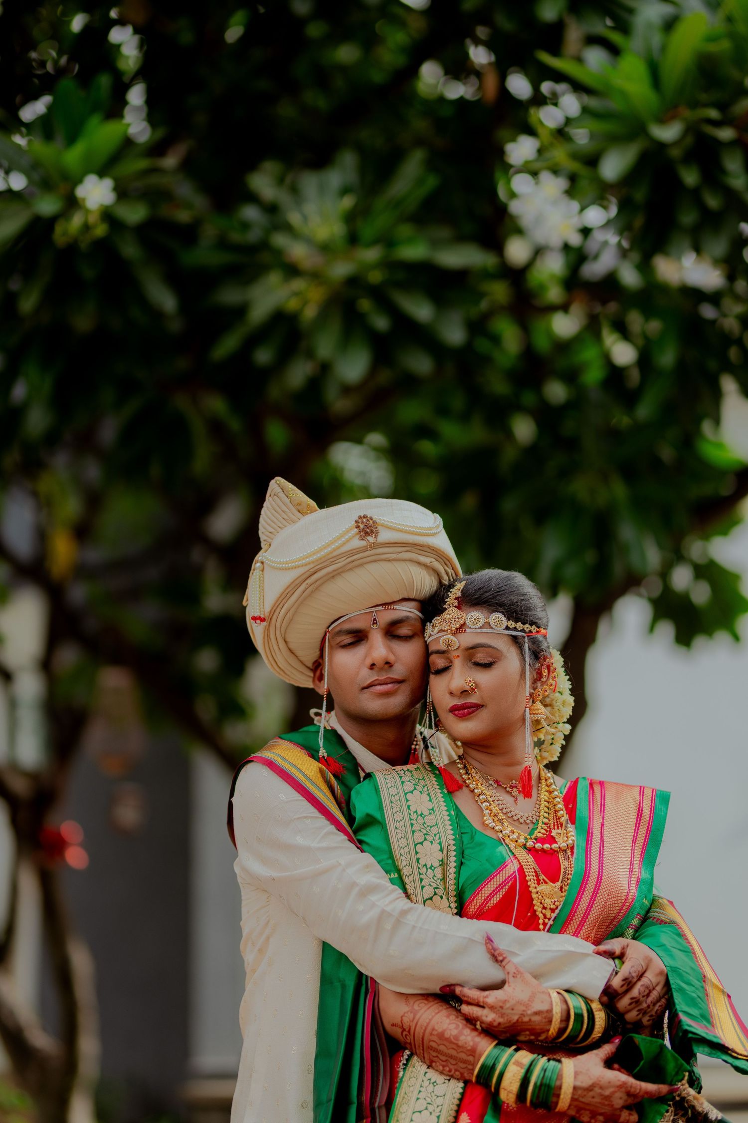Romantic outdoor photoshoot of a couple in traditional Maharashtrian wedding attire embracing under green foliage.
