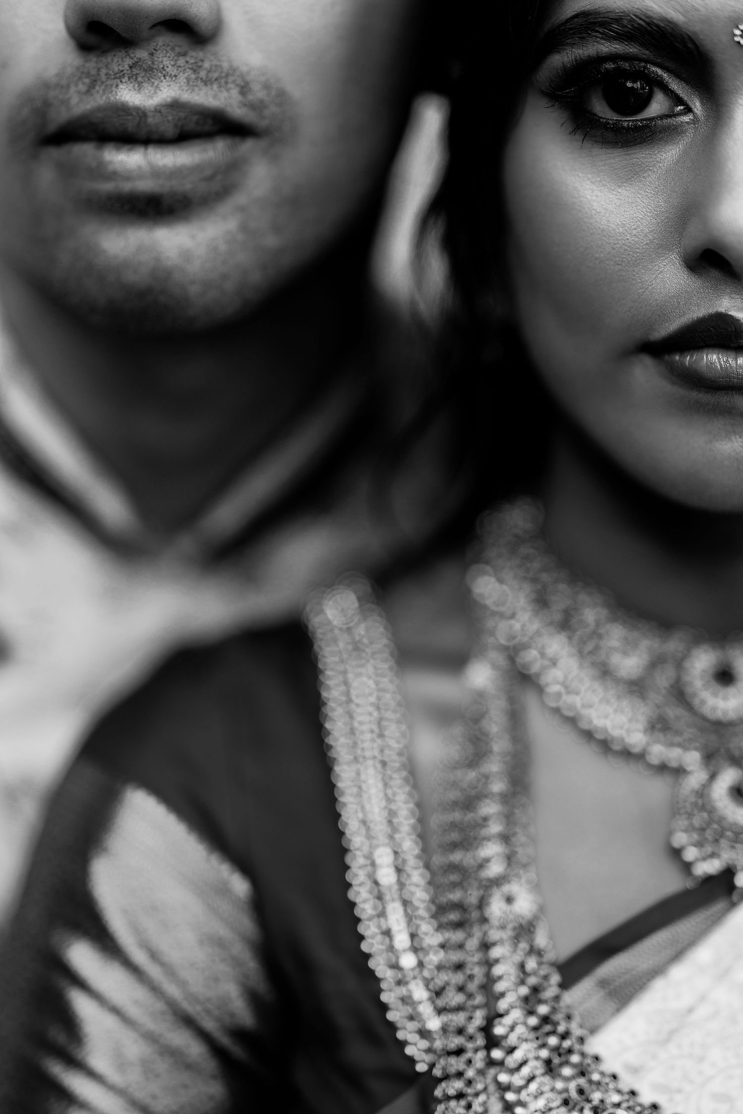 Black and white portrait of an Indian couple in traditional attire, woman wearing ornate jewelry and dark lipstick.