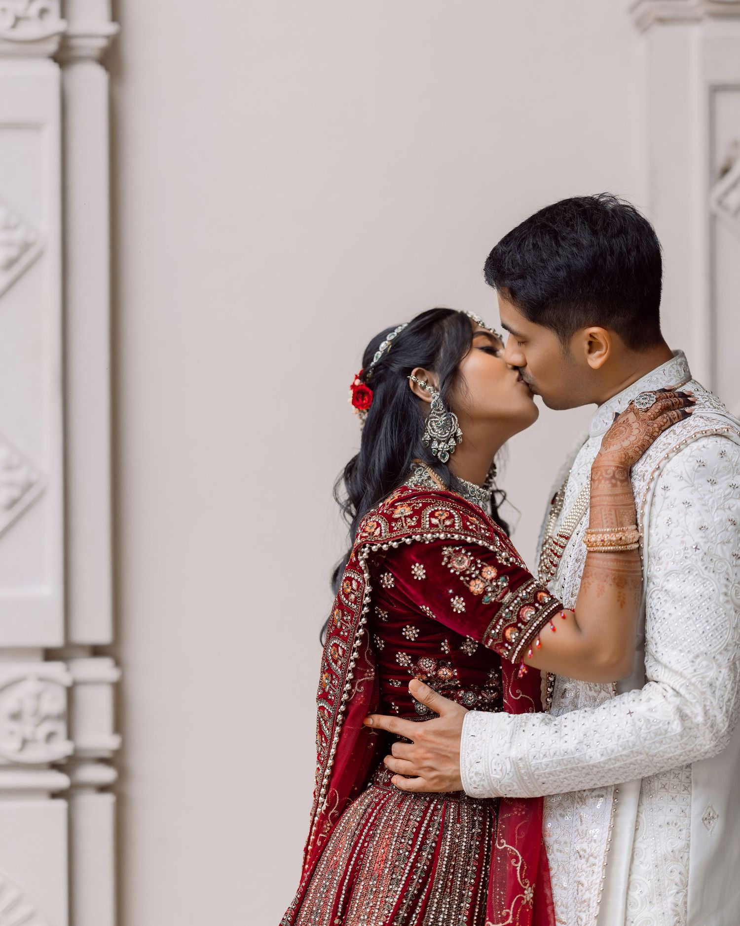 Indian bride in red lehenga and groom in white sherwani share a romantic kiss during their traditional wedding ceremony.