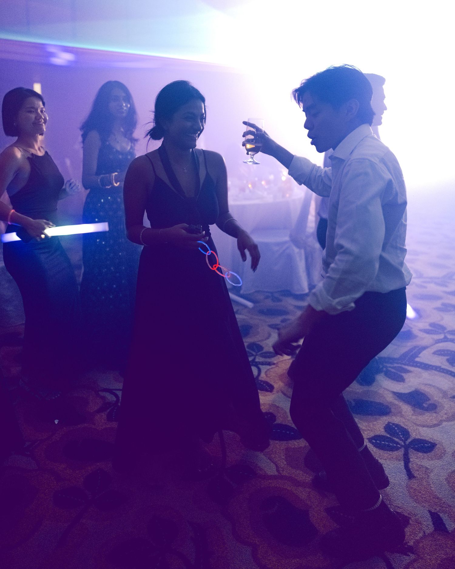 People dancing at a formal party event in a banquet hall with purple lighting and glow sticks.