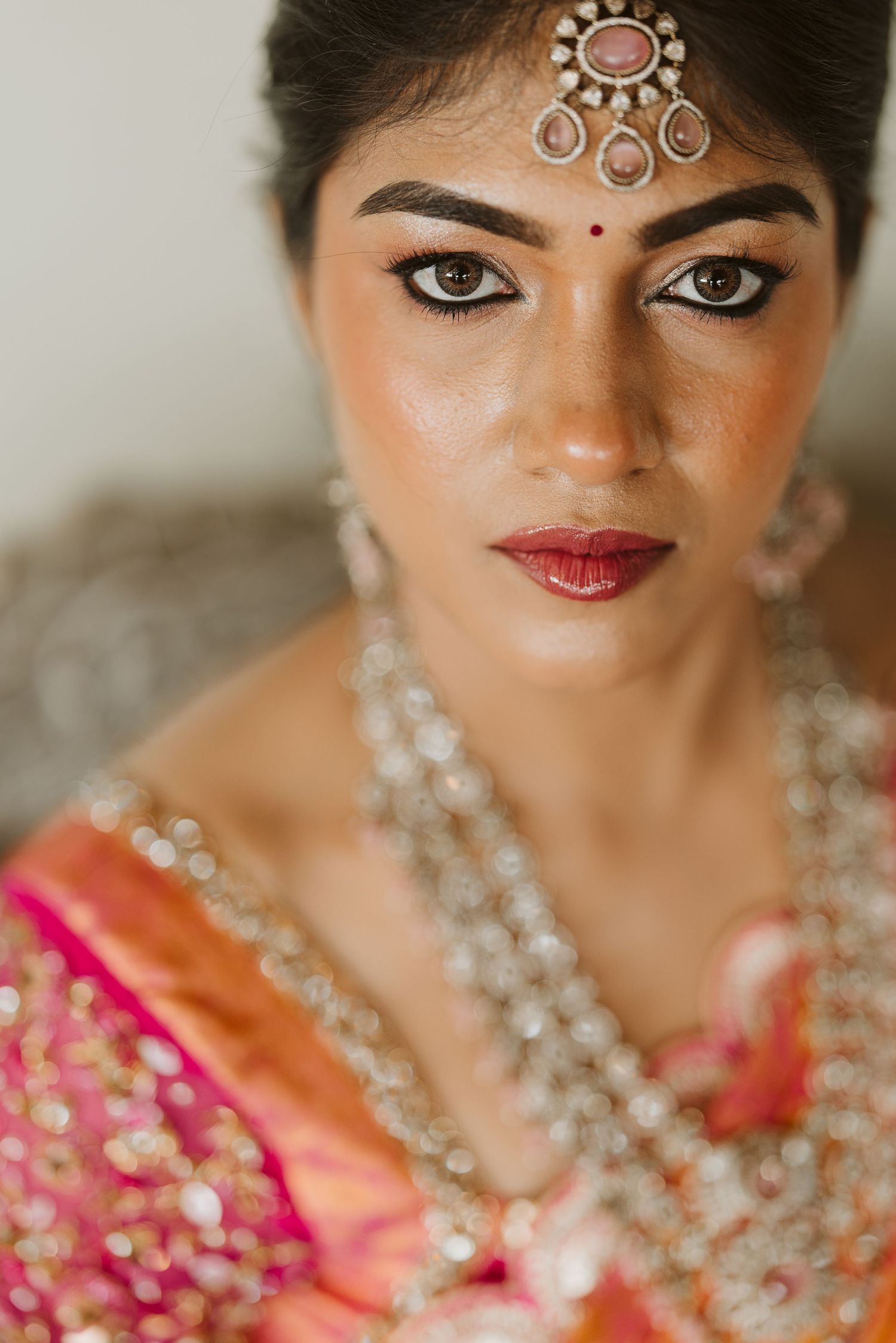 Traditional Indian bridal portrait showing ornate jewelry, maang tikka headpiece and pink sari with detailed makeup.