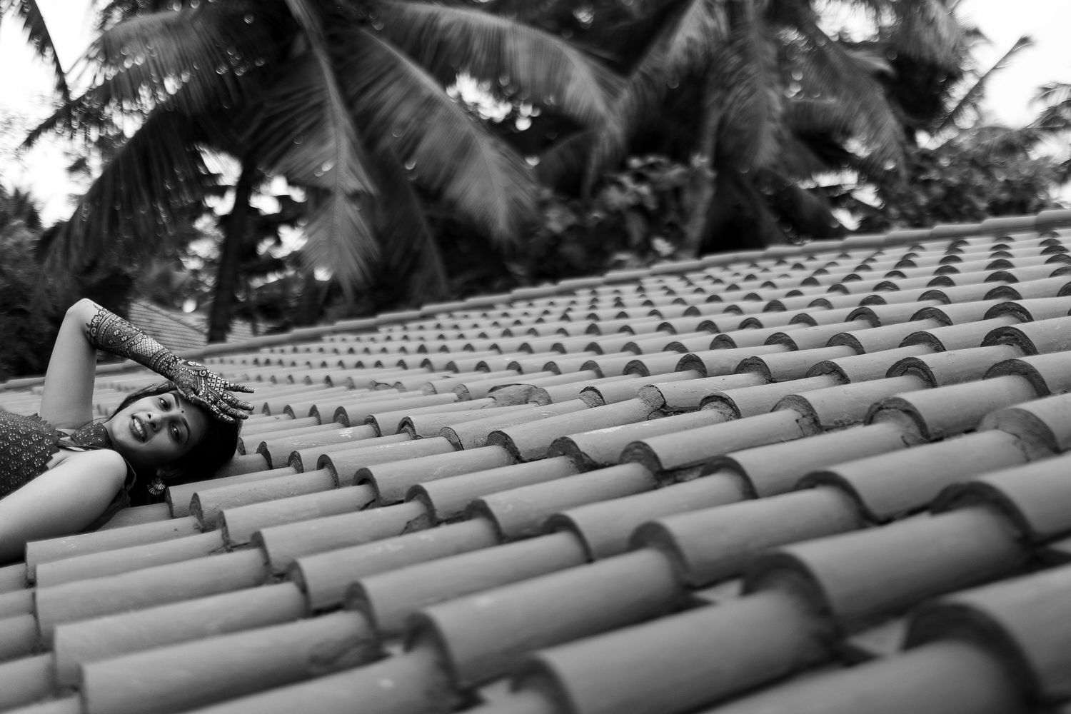 A person lies on curved clay roof tiles in black and white photography with palm trees visible in background.