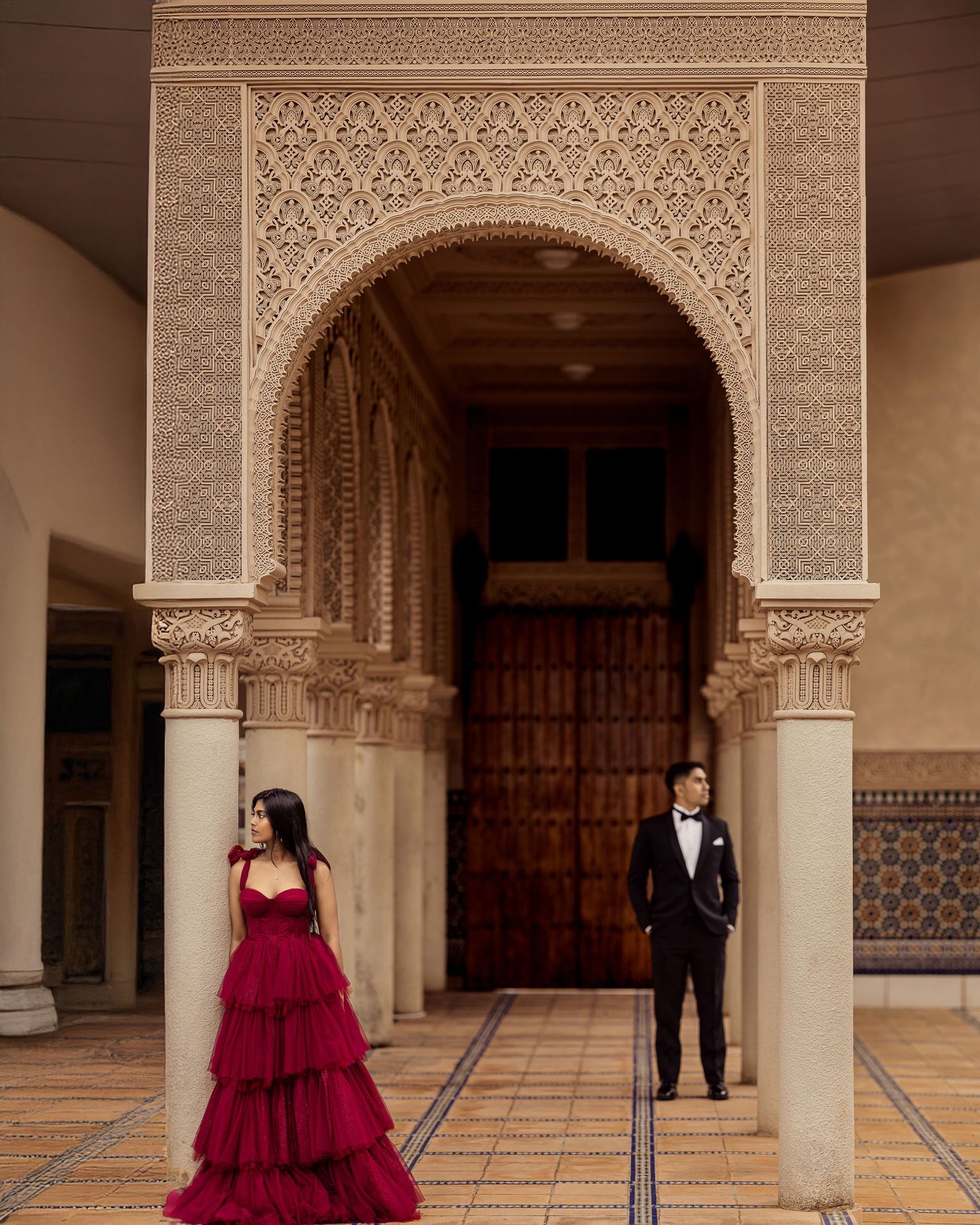 A couple poses in an ornate Moorish-style hallway with arched doorways and intricate carved details.