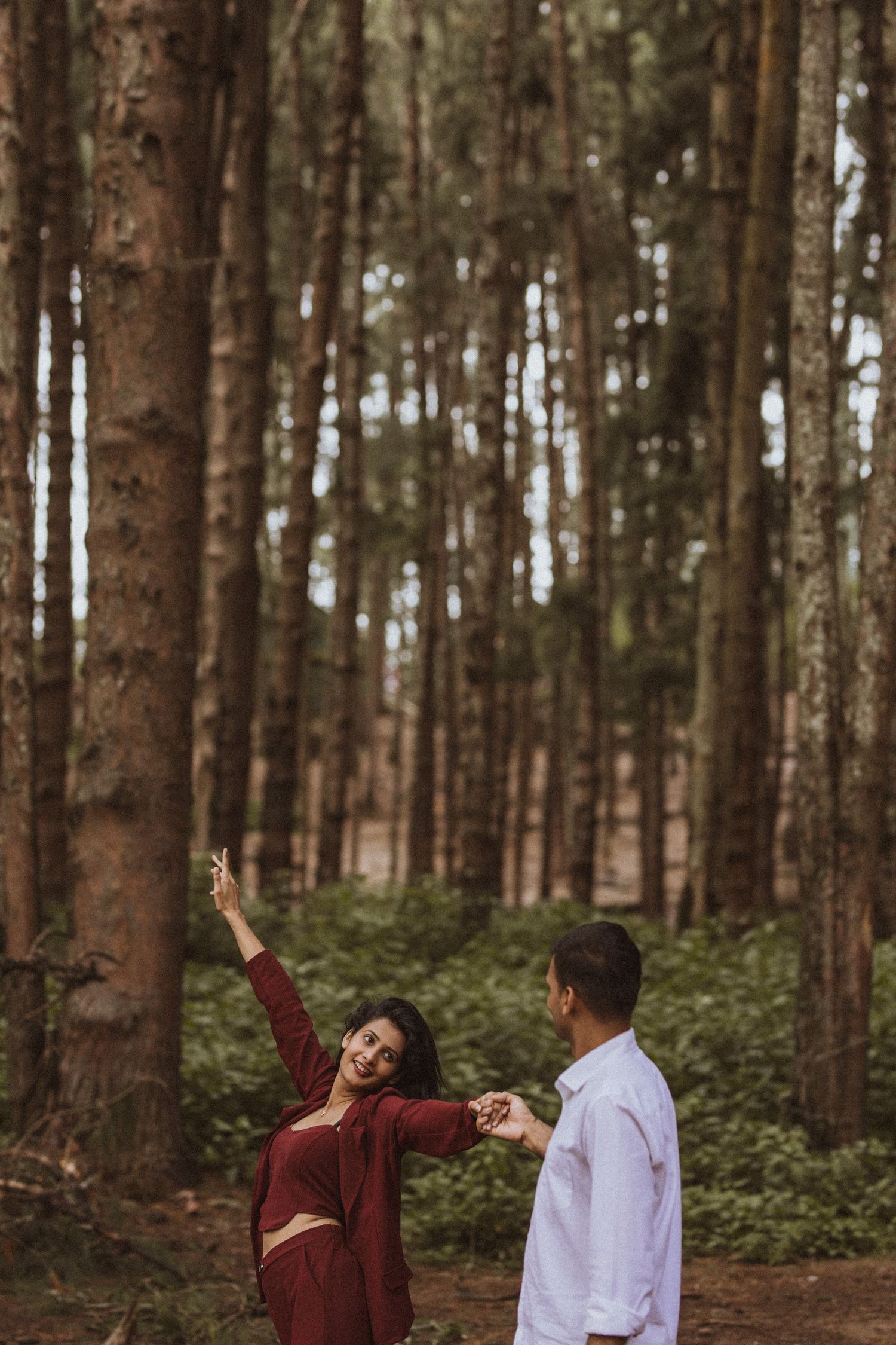 A couple enjoys a playful moment together while walking through a serene pine forest.