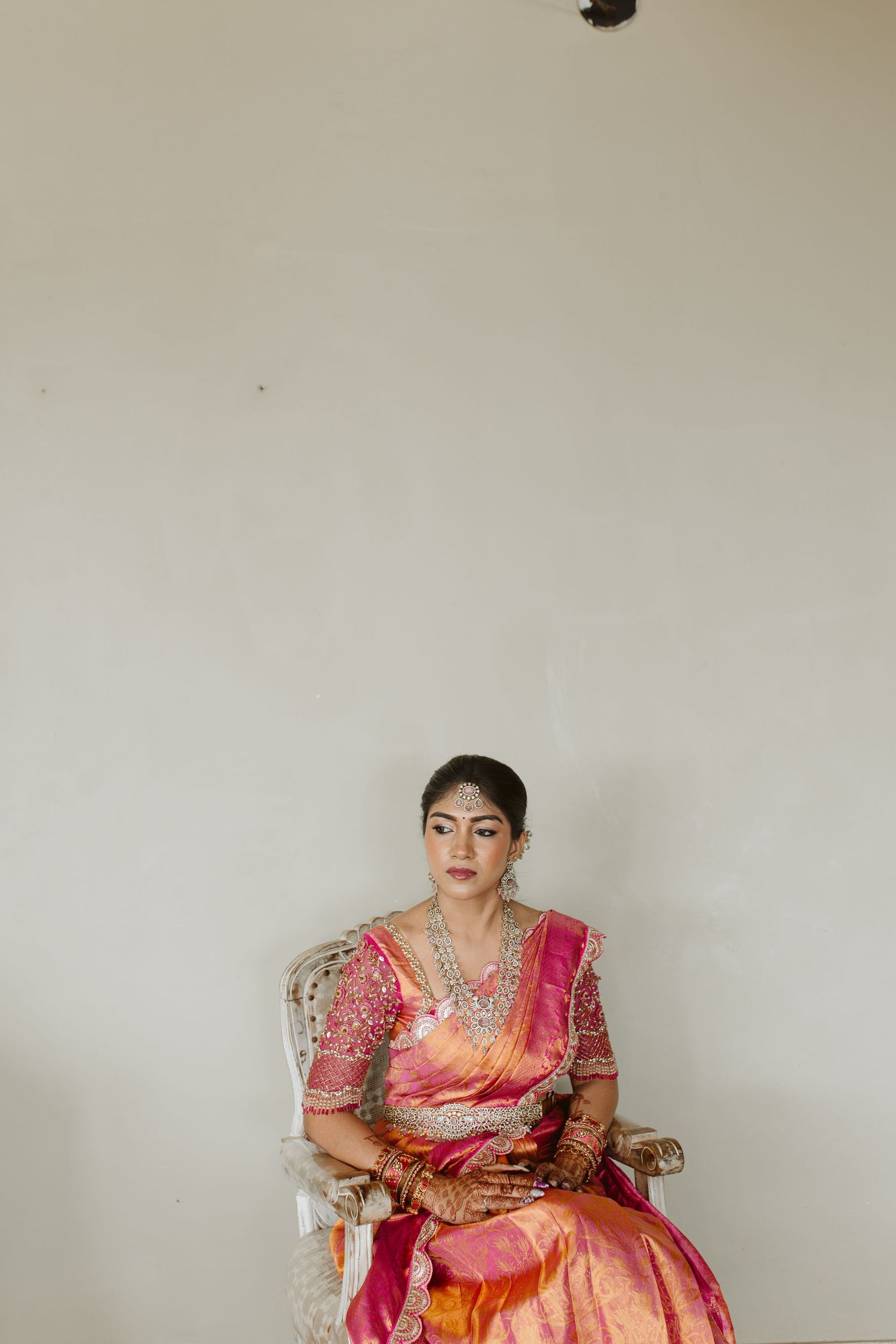 A person in a vibrant pink and orange traditional Indian saree poses against a light colored wall.