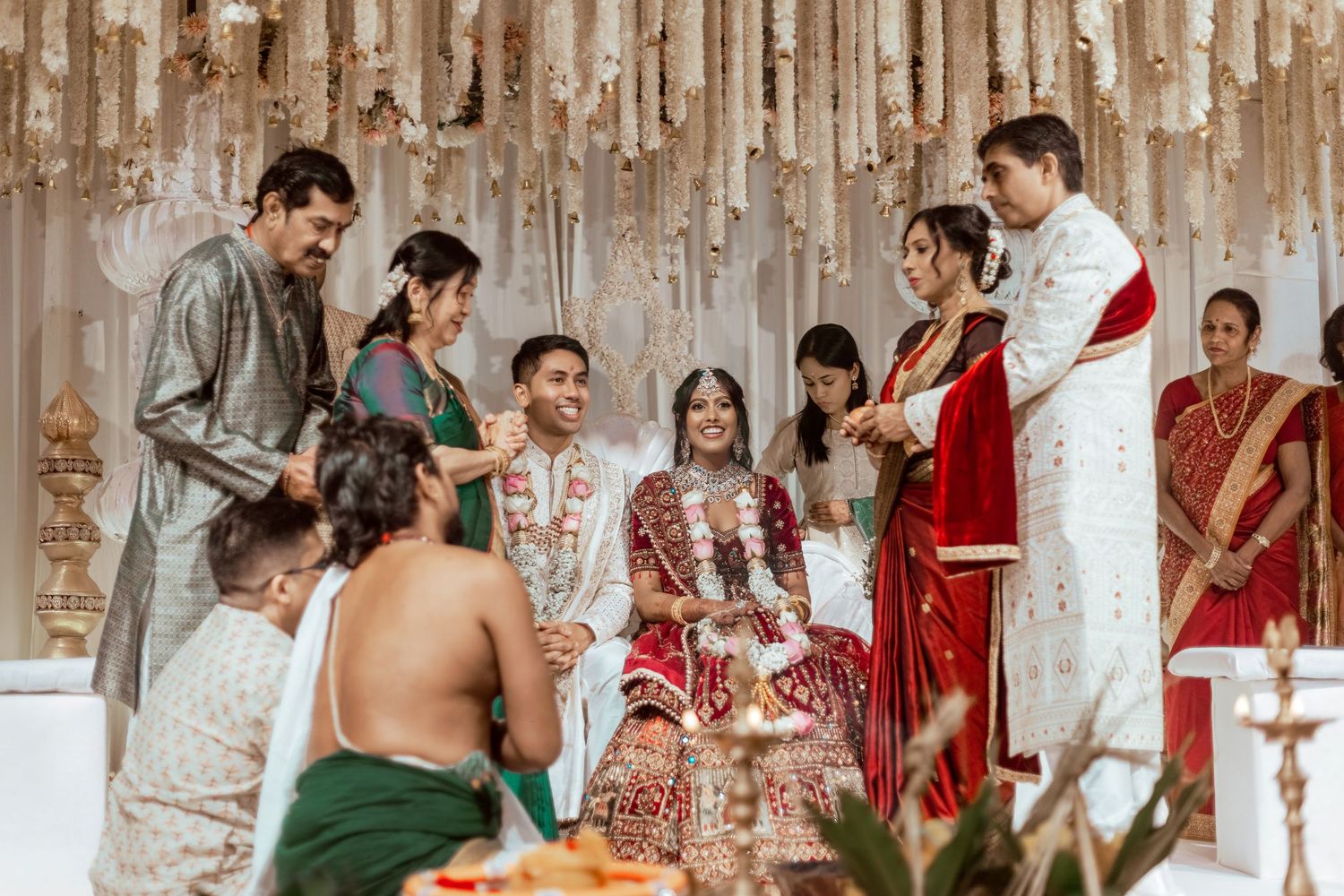 Vibrant Indian wedding ceremony with bride and groom in traditional attire surrounded by family under floral decorations.