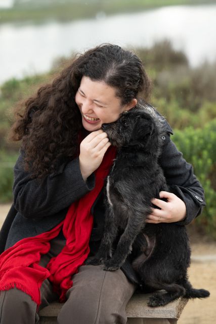 A black dog shares a joyful moment with someone wearing a red dress outdoors.