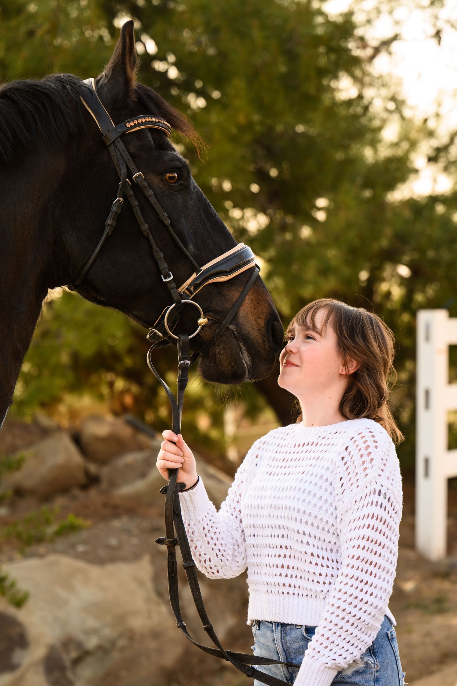 A beautiful black horse and person in white sharing an affectionate moment at sunset with white fencing in background.