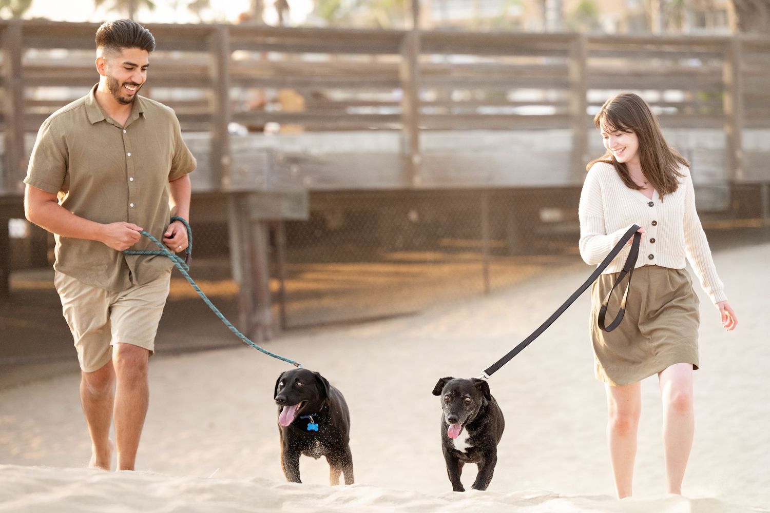 Two happy dogs and their owners walking together on Newport Beach during golden hour.