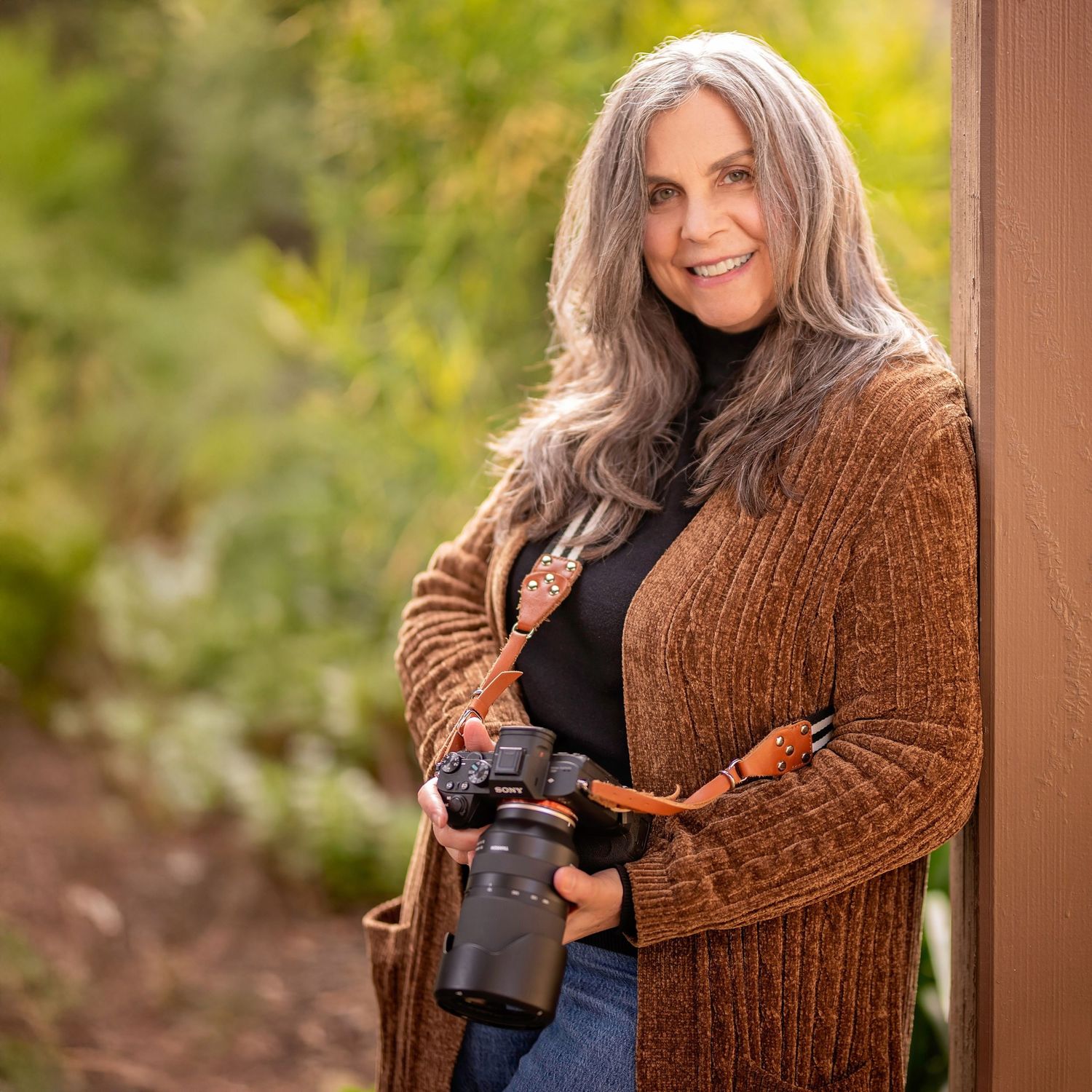 Person in brown sweater holding professional camera equipment outdoors.