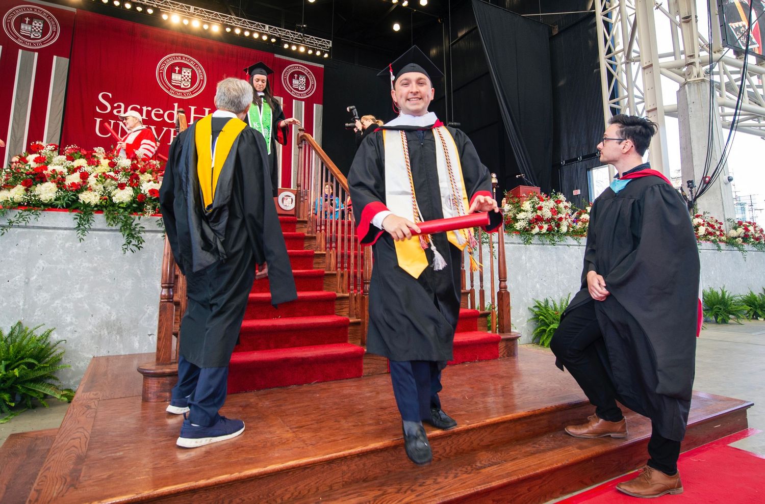Graduates posing for photos in front of festive holiday decorations and red backdrop.