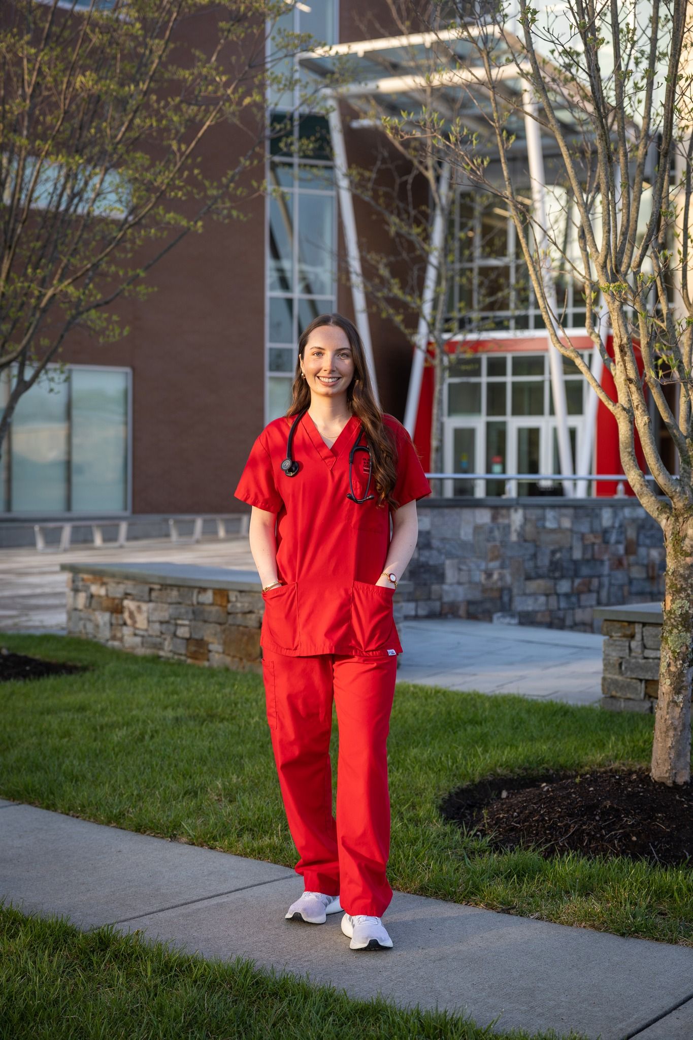 Healthcare professional in bright red scrubs walks along a paved pathway outside a medical building.