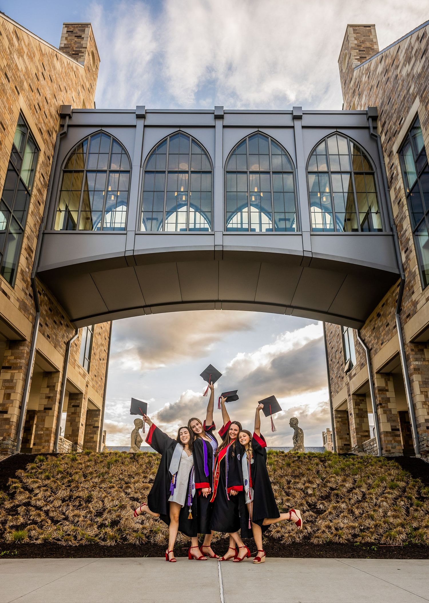 Graduates throw caps in celebration beneath an architectural bridge connecting campus buildings.