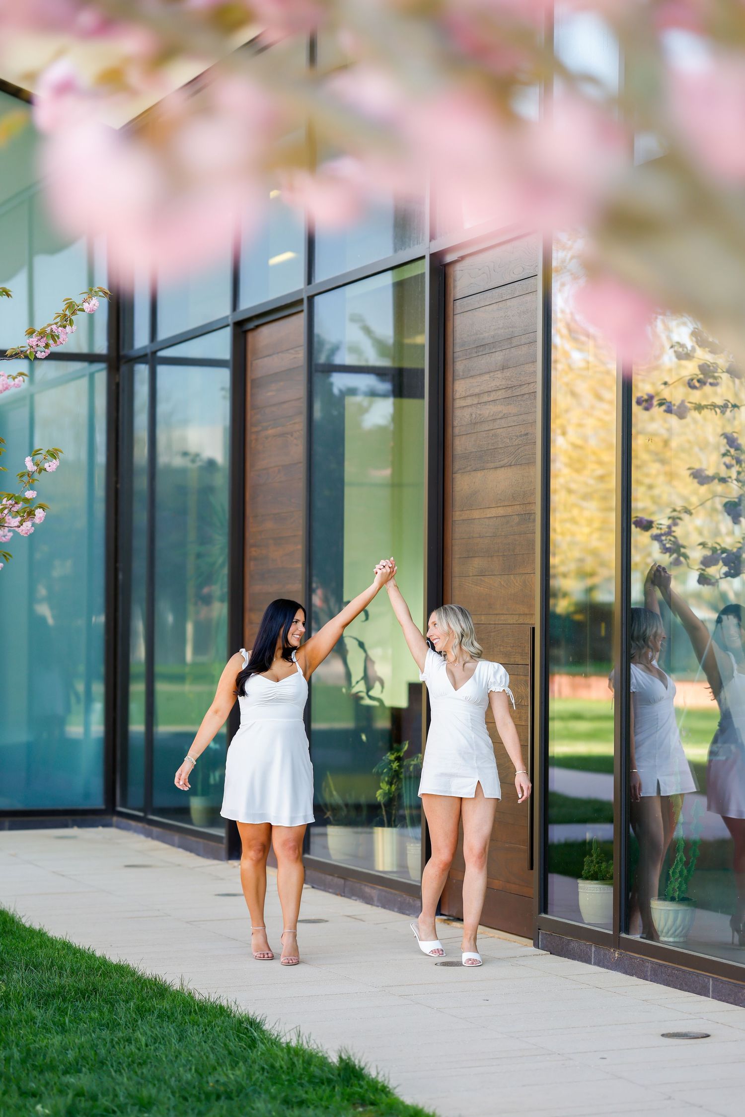 Cherry blossoms frame graduates celebrating outside a modern glass building.