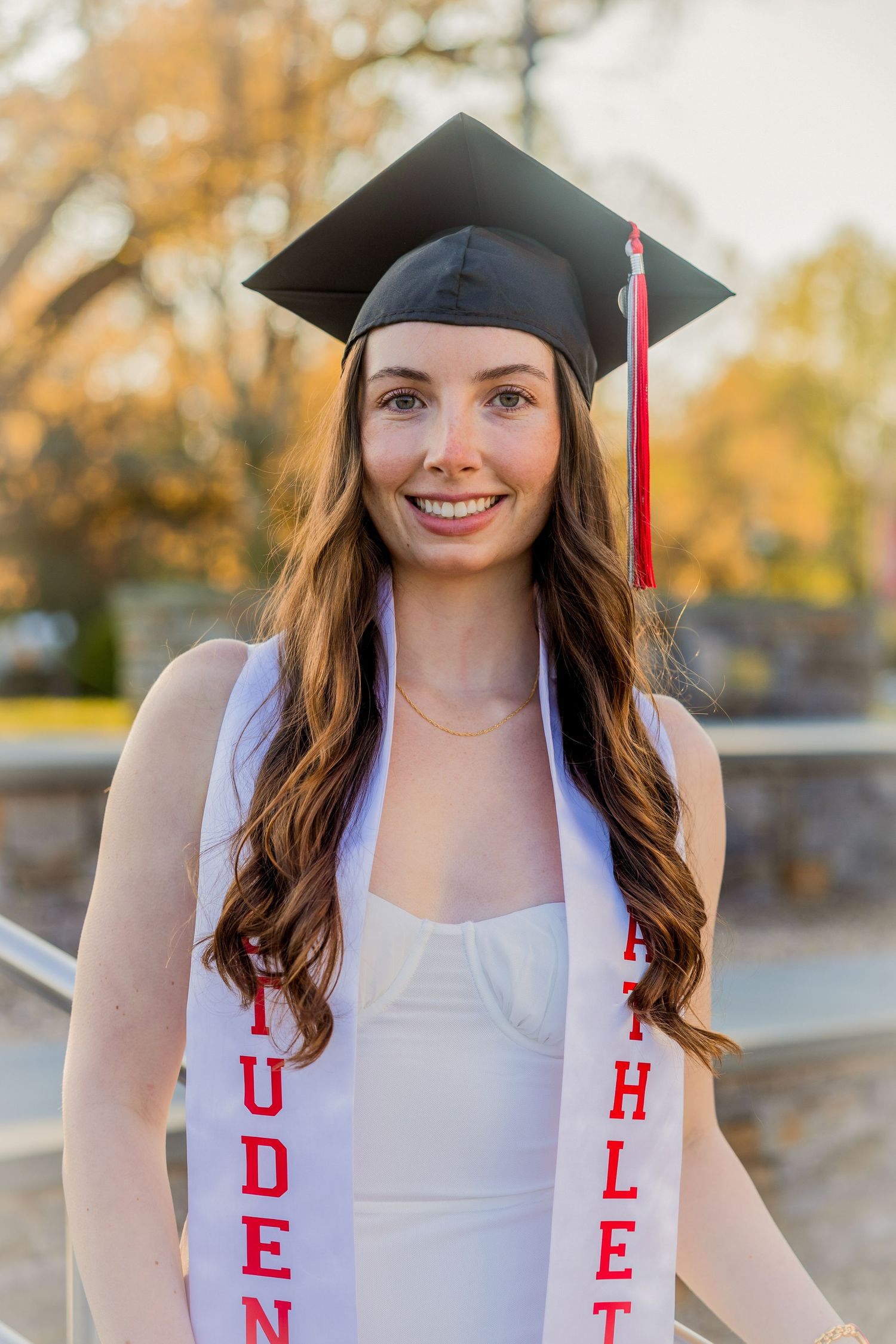 Graduate in cap and gown smiles during outdoor graduation photoshoot.