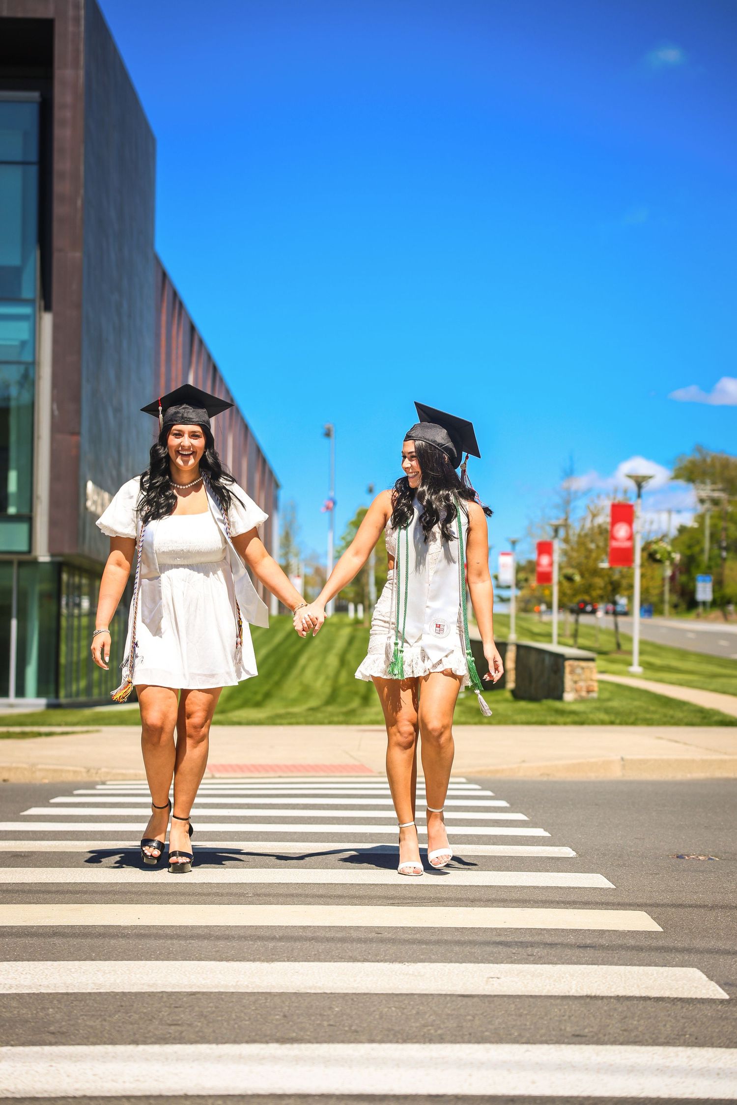 Graduates in caps and gowns walking across a crosswalk on campus.