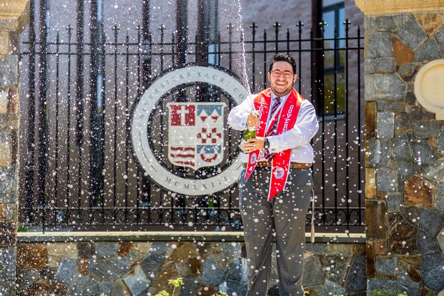 Winter graduation scene outside historic building with snow falling and decorative iron gates.