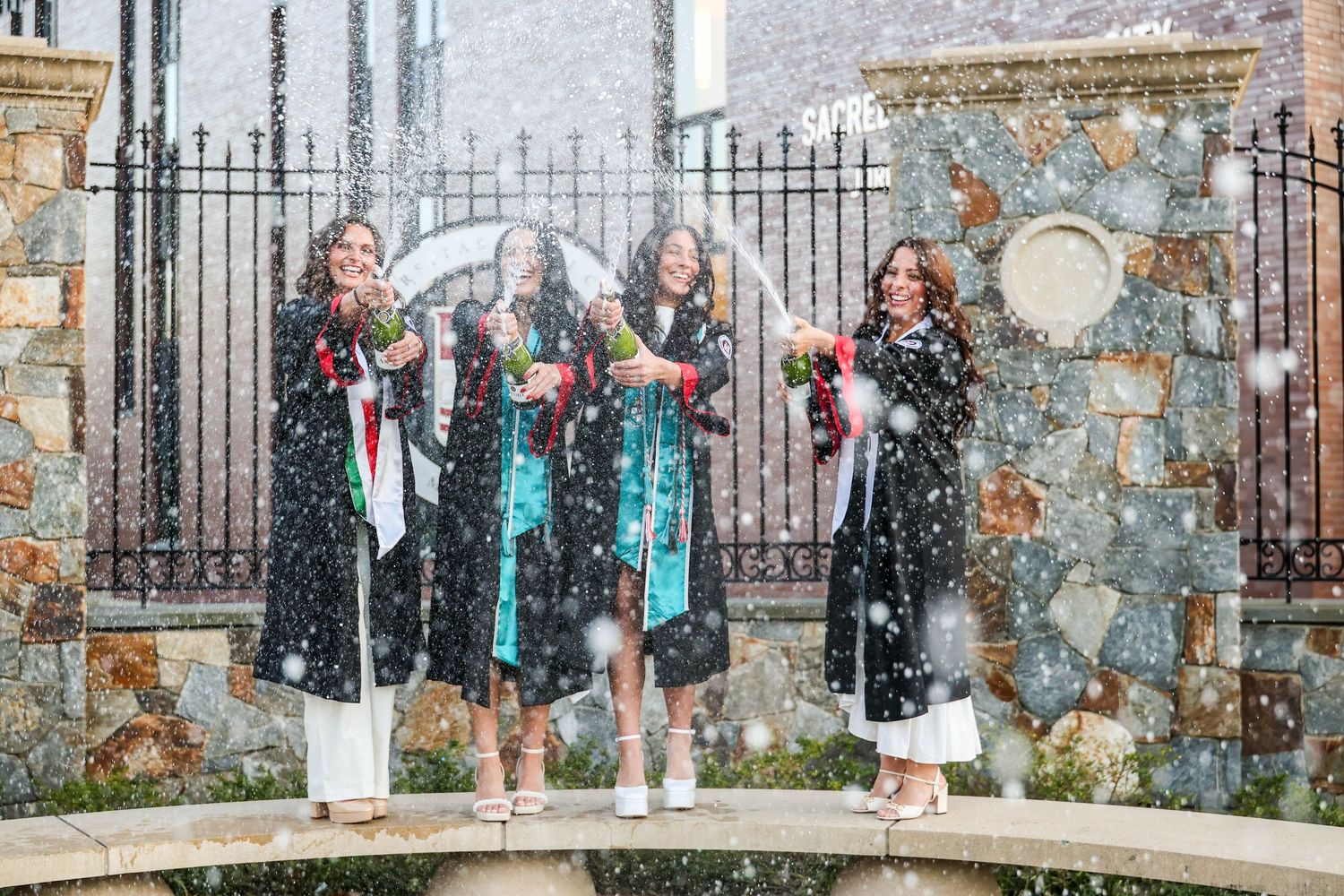Group poses together in front of decorative iron gates wearing graduation attire.