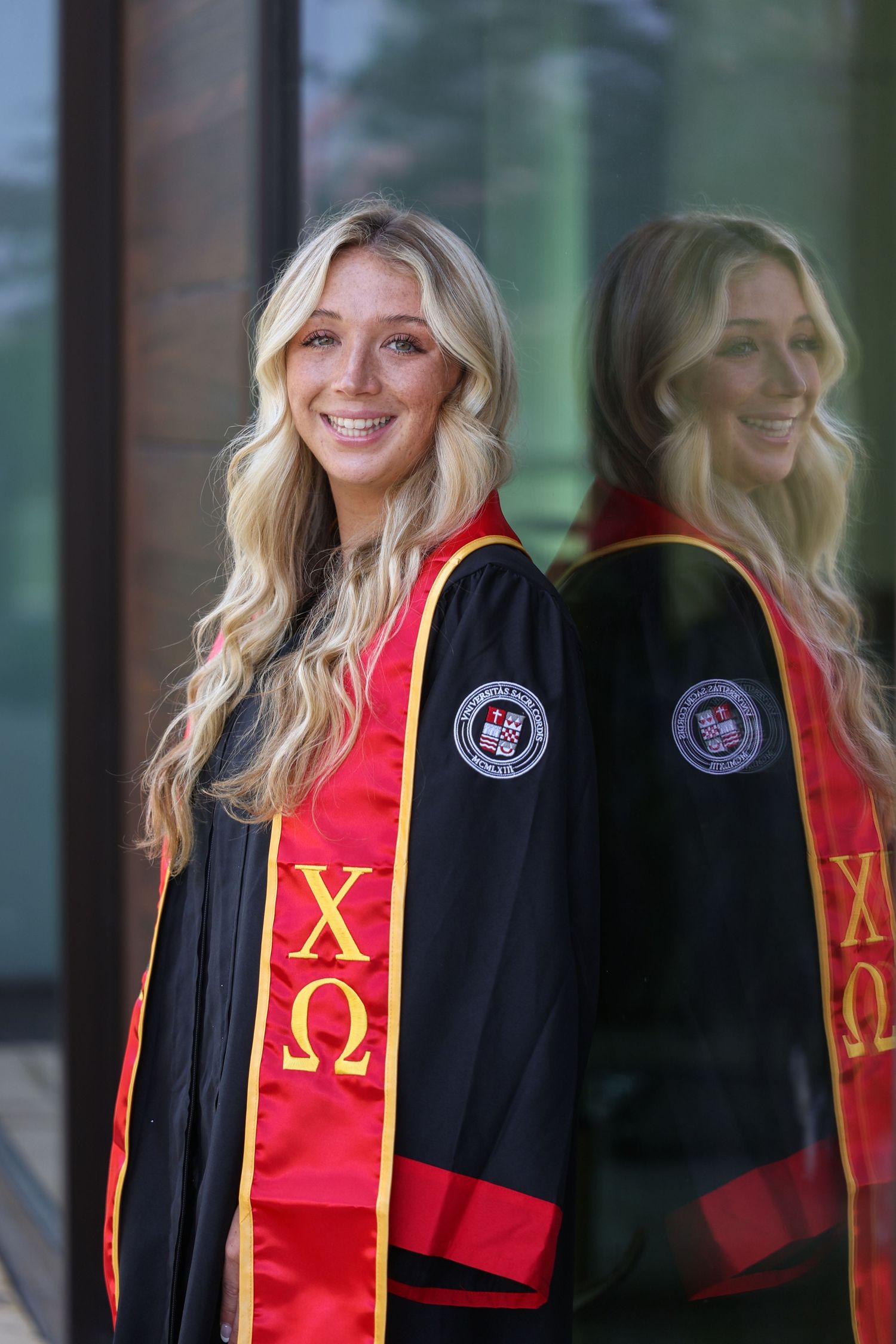 Graduate wearing sorority stole and graduation regalia poses for portrait.