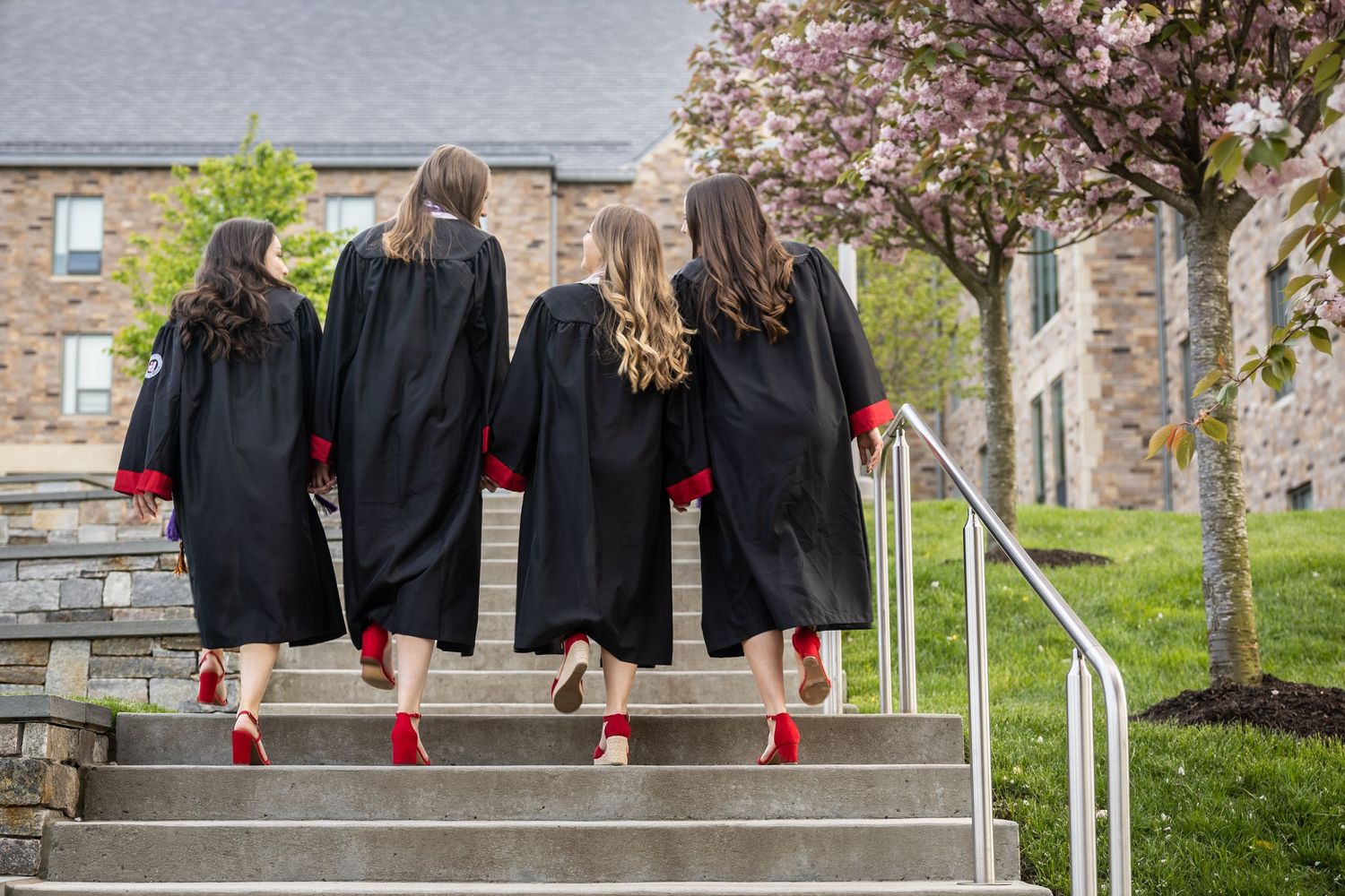 Graduates in black robes and red shoes descend stone steps together.