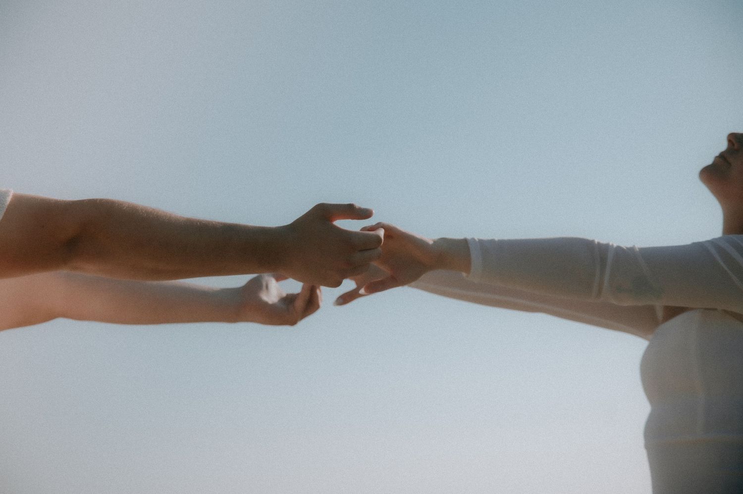 A blurred silhouette of two people reaching out to hold hands against a light background.