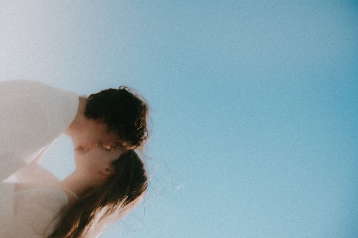 Dreamy silhouetted figures embrace against a soft blue sky background in an artistically blurred composition.