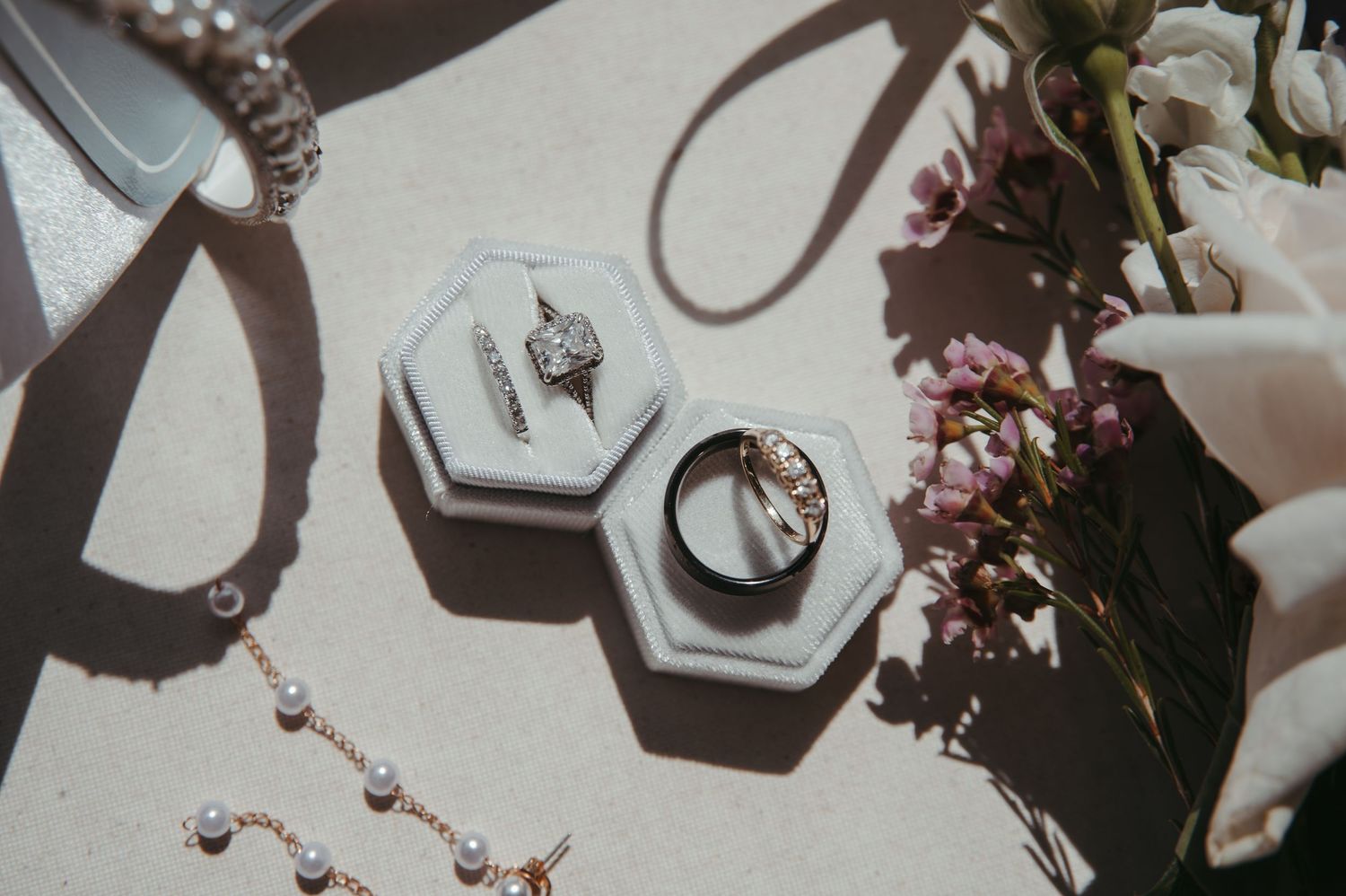 Engagement rings and jewelry displayed in hexagonal holders next to flowers and delicate accessories in natural light.