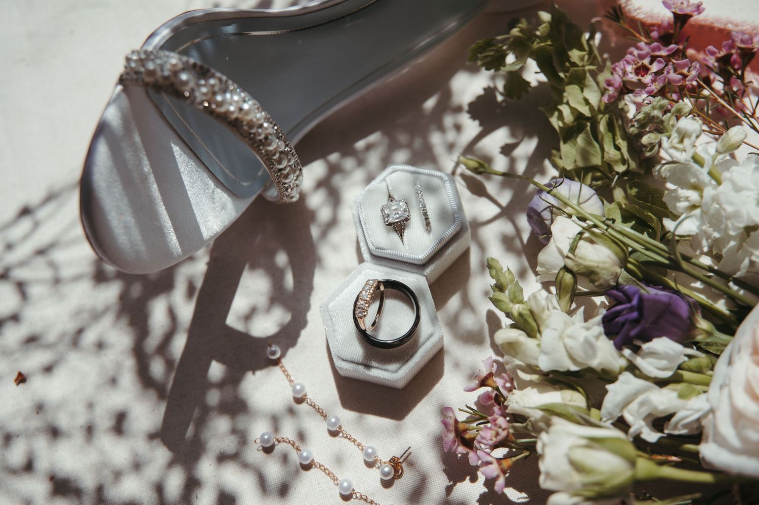 Wedding rings nestled in a hexagonal box surrounded by delicate flowers and casting soft shadows.