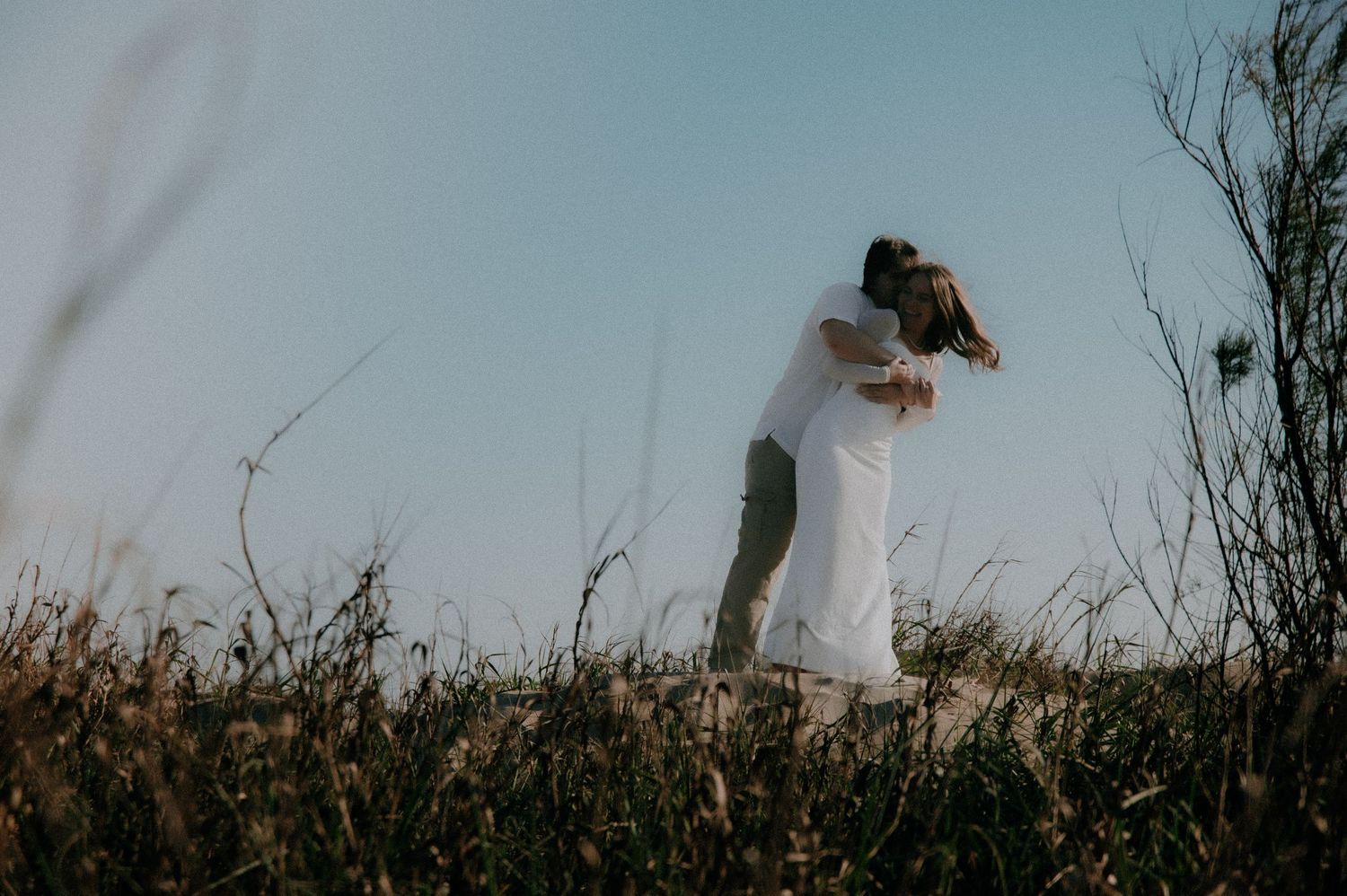 A person in a white dress walks through a misty field of tall grass at dusk creating an ethereal silhouette.