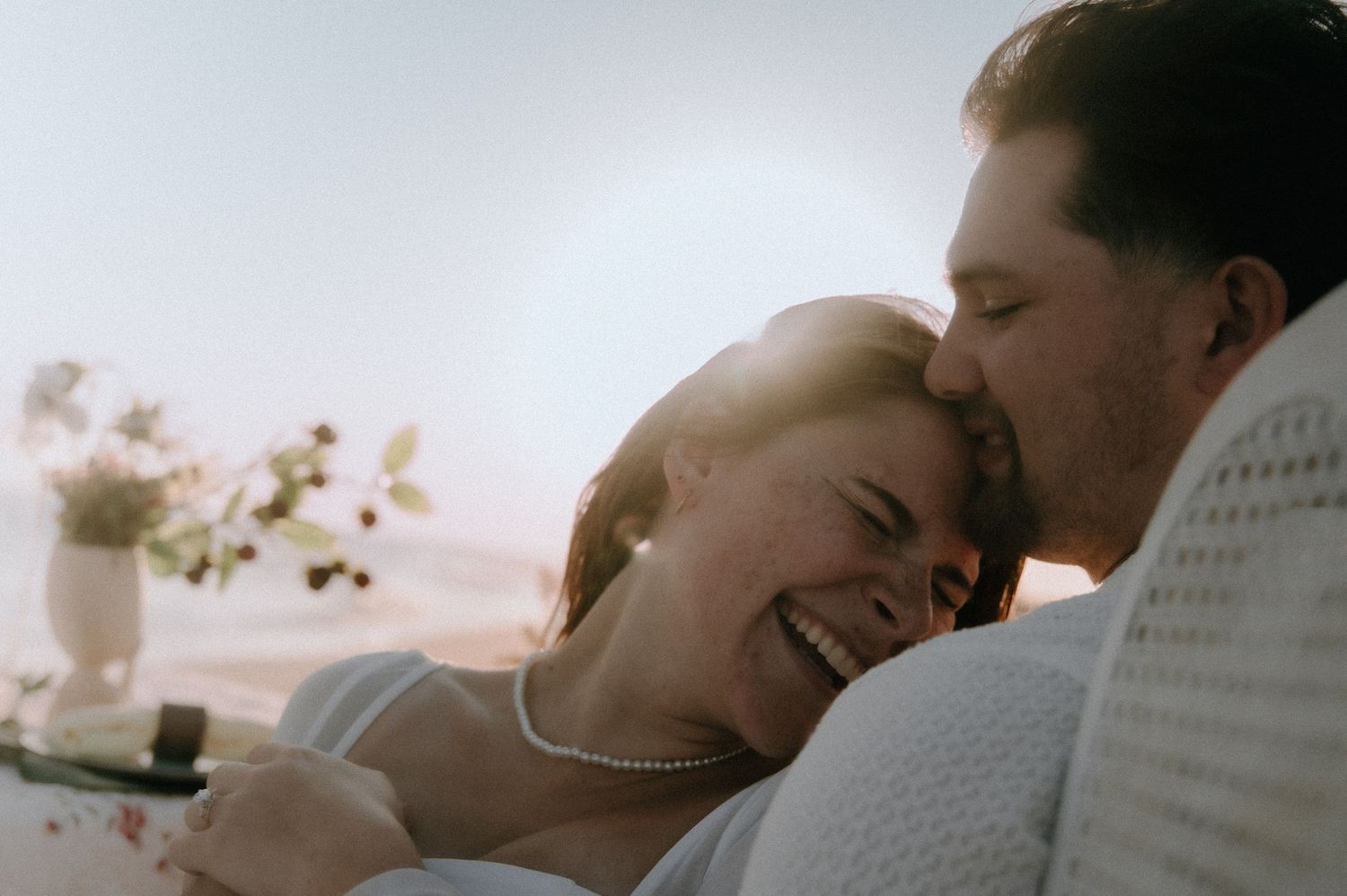 A couple shares an intimate embrace in a romantic sunset silhouette against a dreamy golden sky.