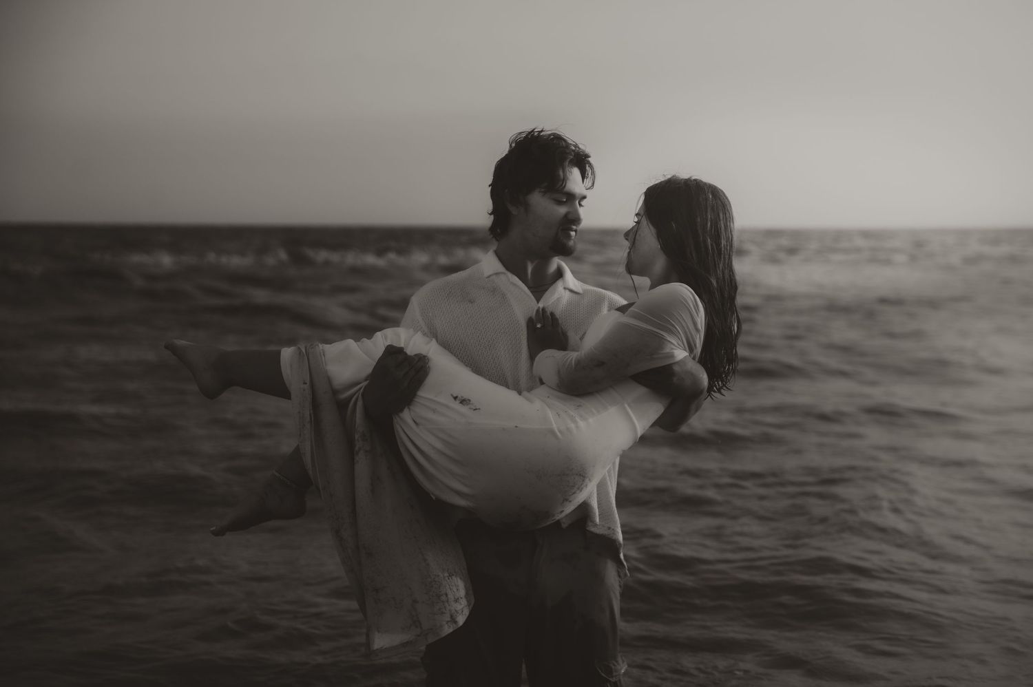 A series of black and white photographs showing a couple embracing and dancing along a misty oceanfront at sunset.